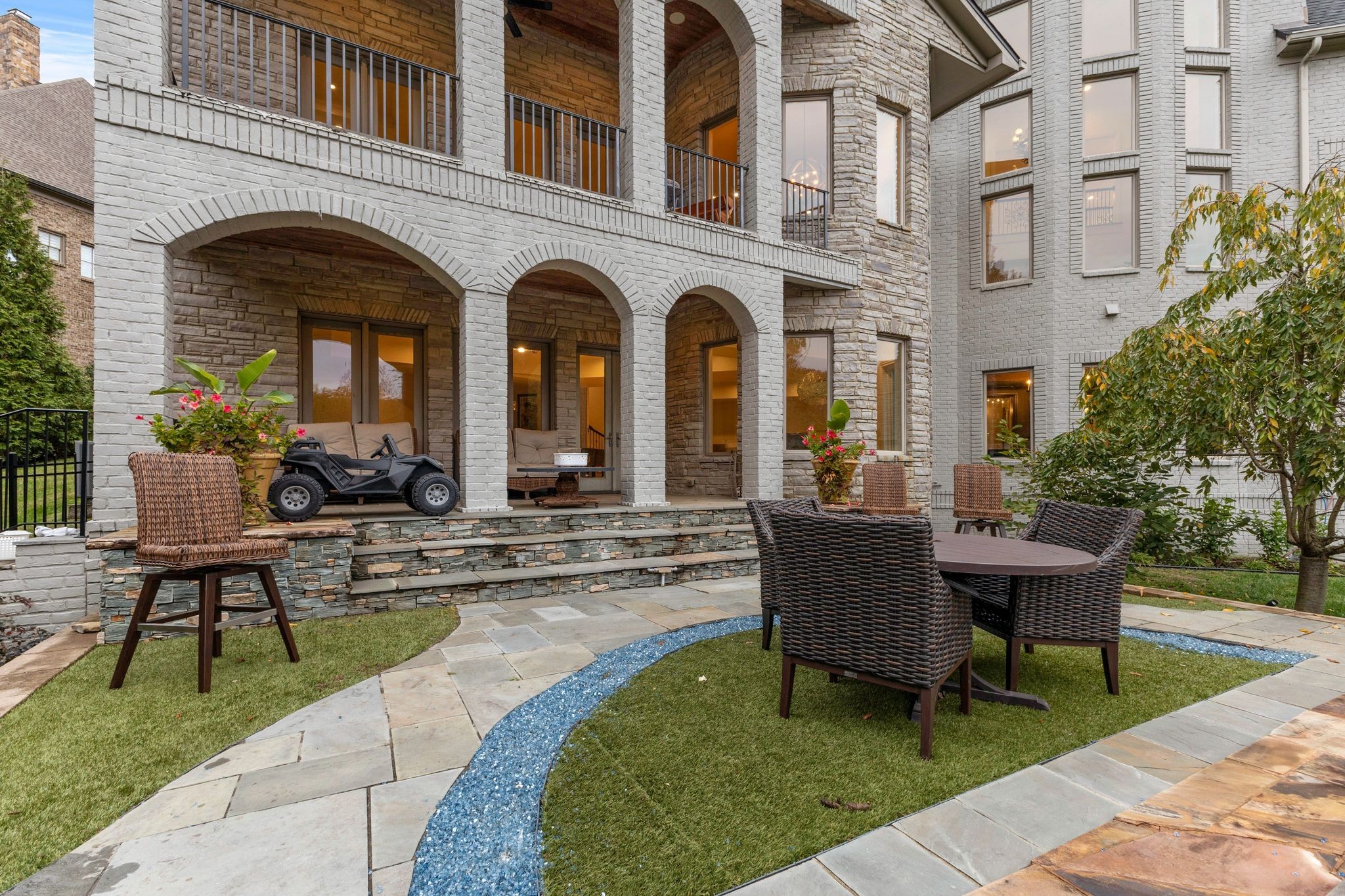 Rear patio with arched brick porches, stone paving, and outdoor seating.