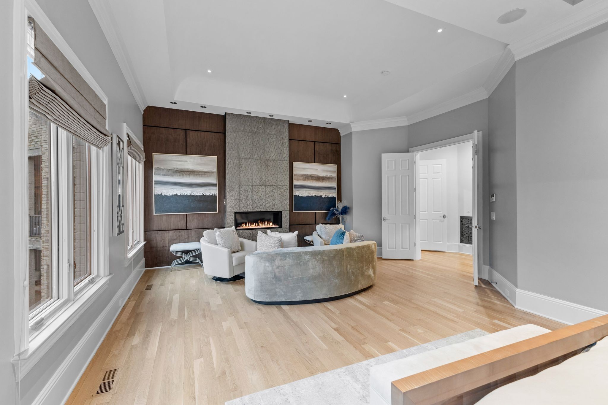 Living room with curved sofas, tall windows, and a fireplace in a dark wood feature wall.