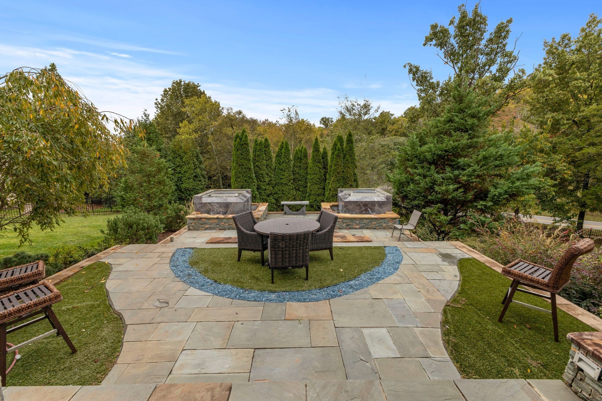 Stone patio with a round wicker dining set, two raised stone features, and mature trees for privacy.