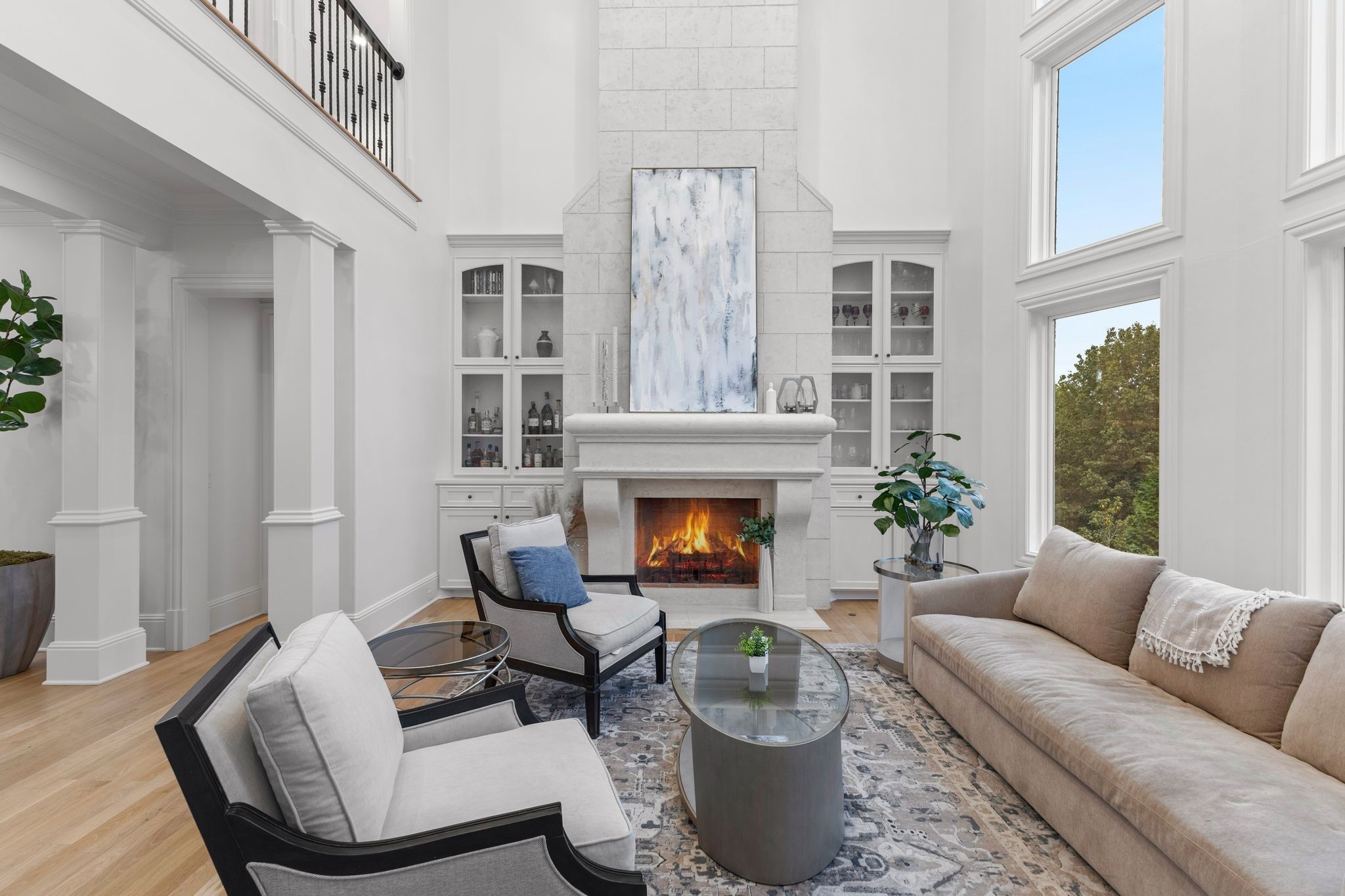 Double-height living room with a tall stone fireplace, built-in cabinets, and large windows.