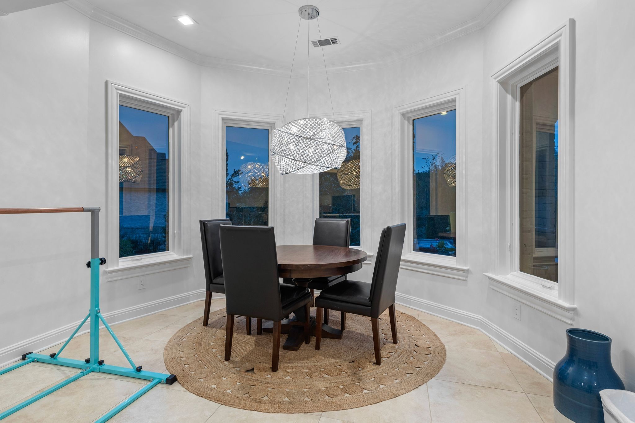 Dining room with a round wood table, black chairs, woven rug, and sculptural pendant light.