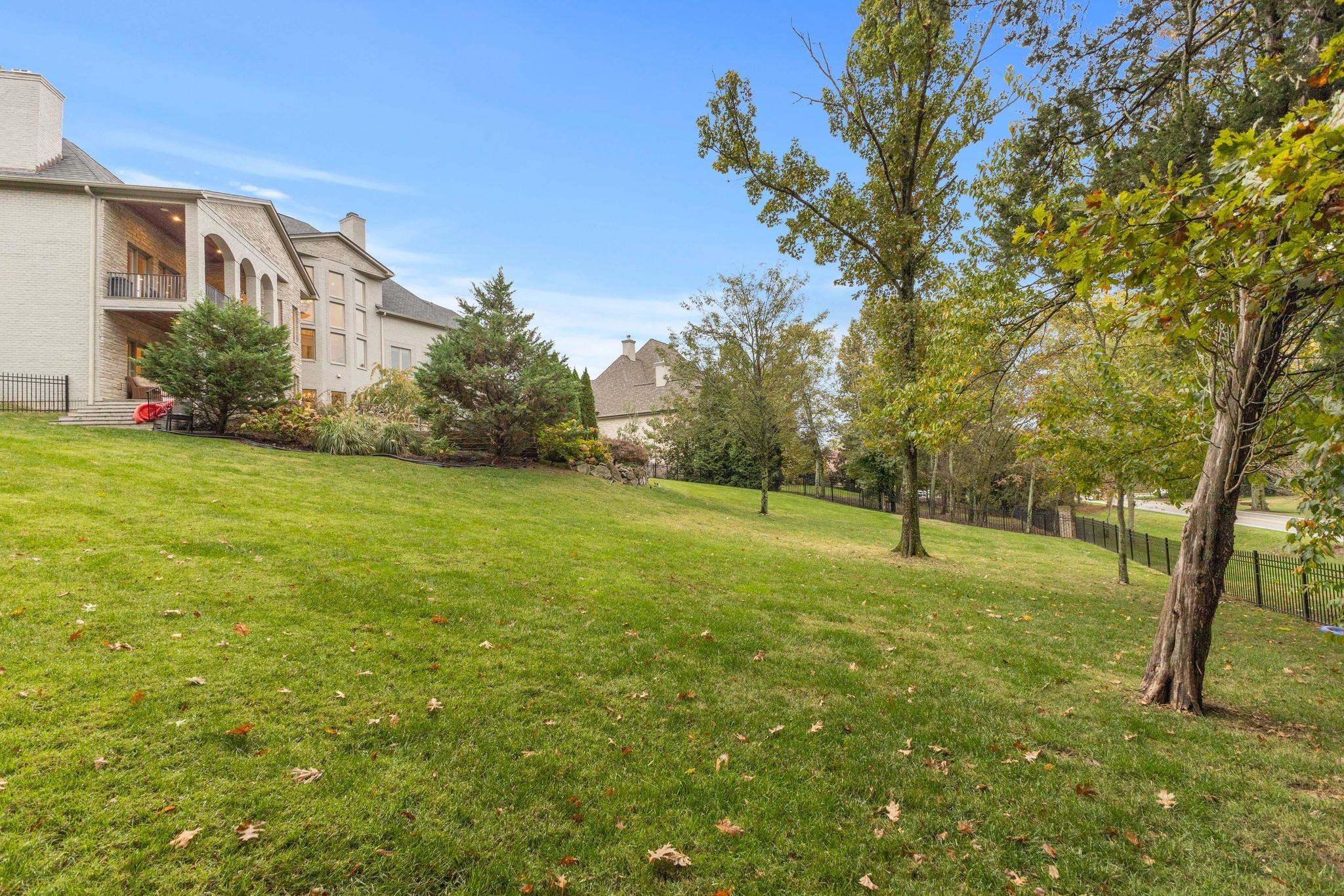 Large brick home with arched balconies above a sloping lawn shaded by mature trees.