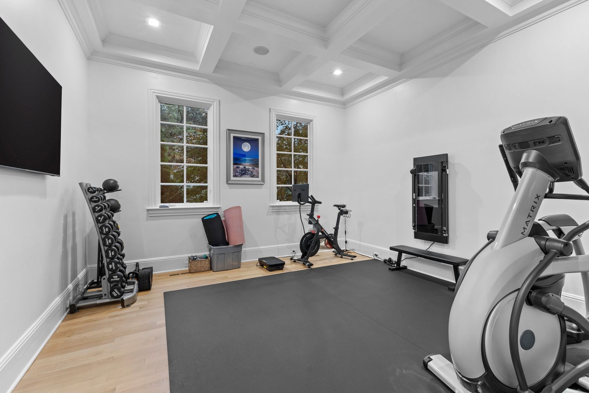 Home gym with a coffered ceiling, dumbbell rack, and cardio equipment.