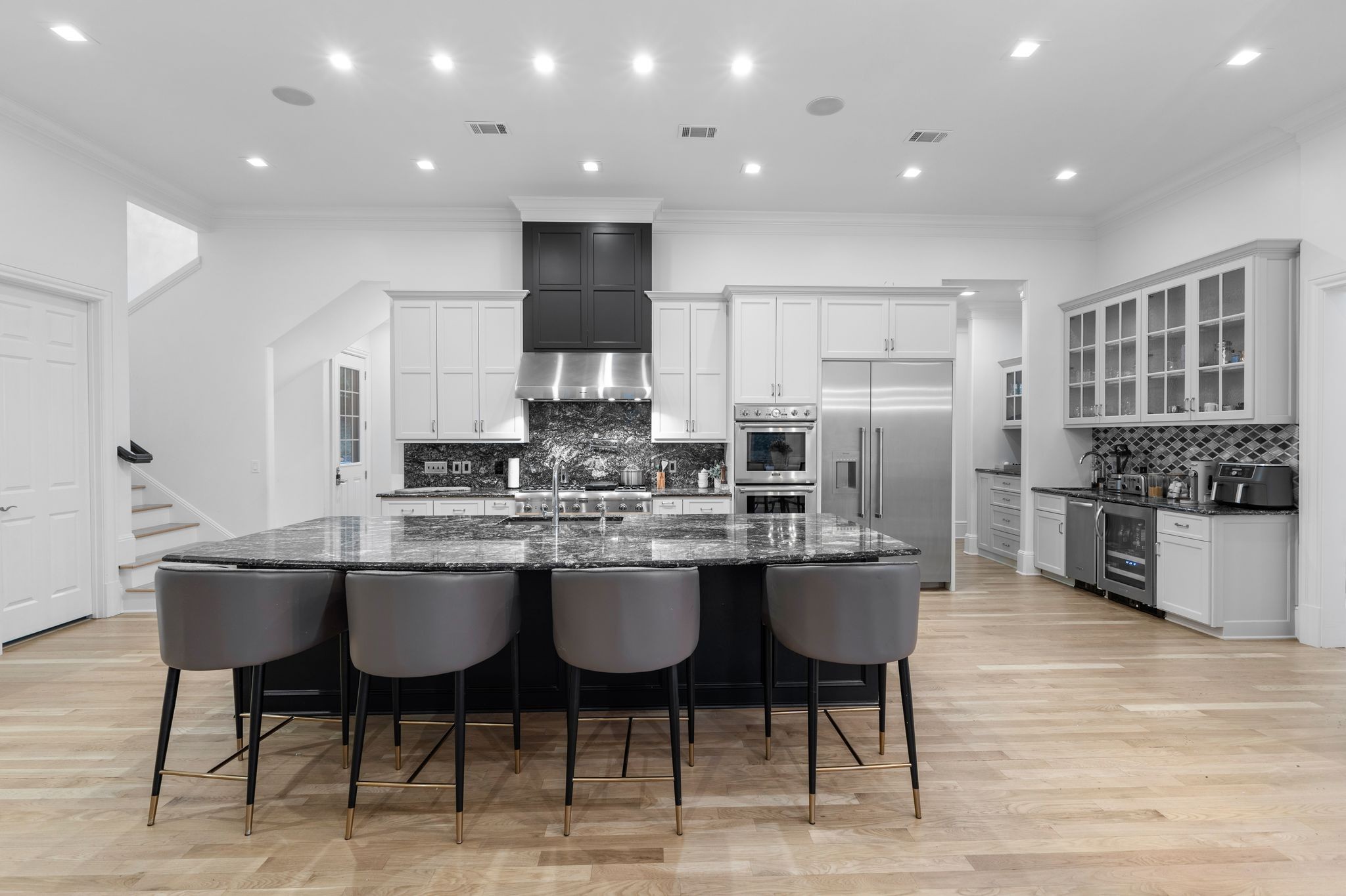 Kitchen with a large dark stone island, four bar stools, white cabinets, and stainless steel appliances.