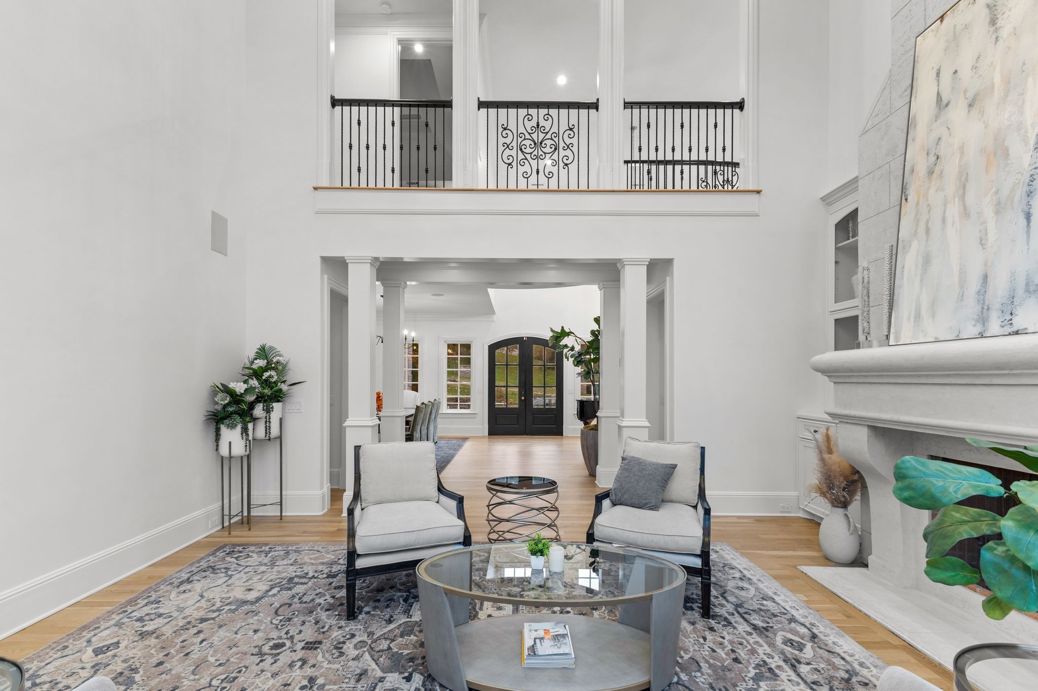 Living room with a high ceiling, wrought-iron balcony railing, stone fireplace, and black double doors.