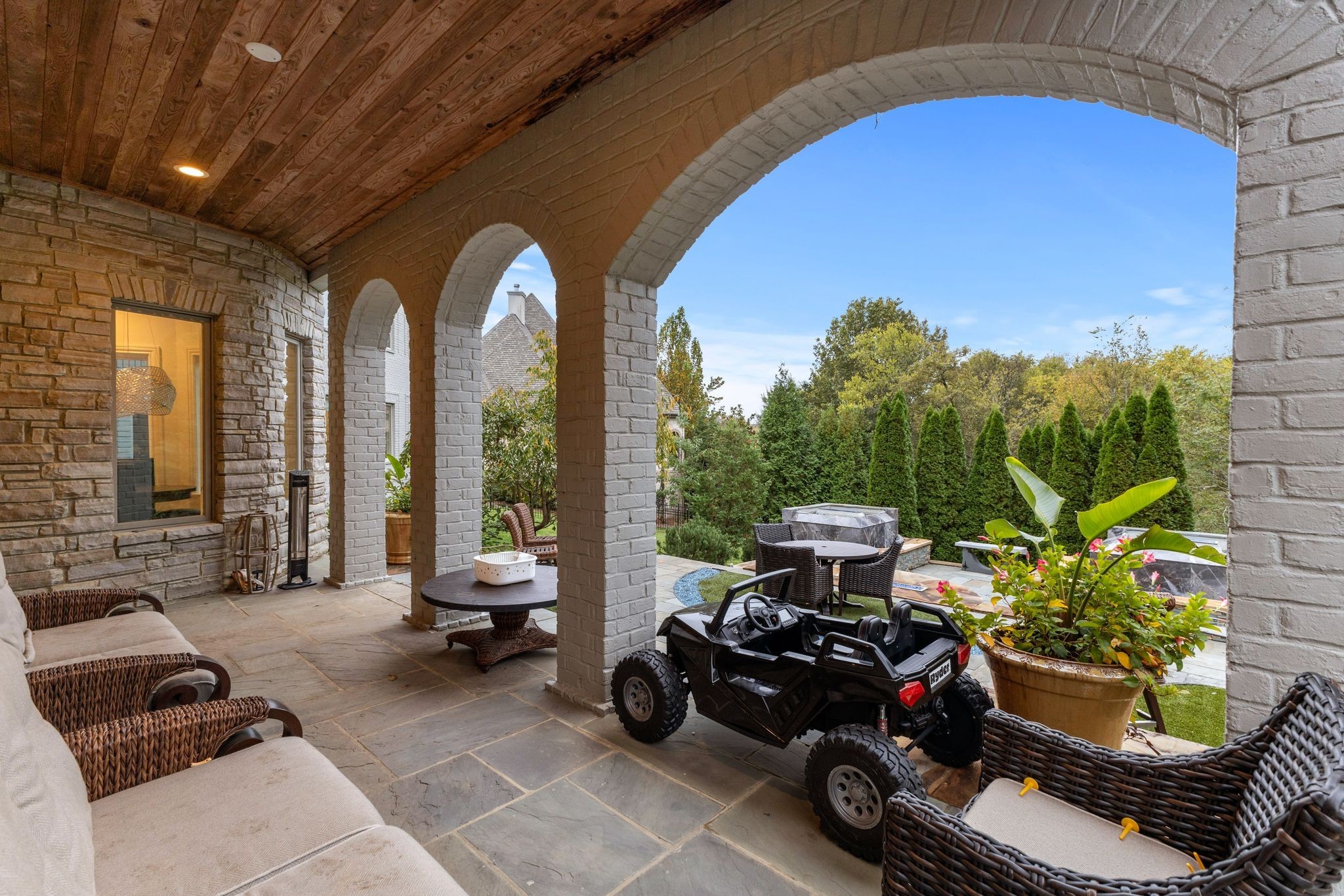 Covered stone patio with brick arches, wicker seating, and a small off-road vehicle.