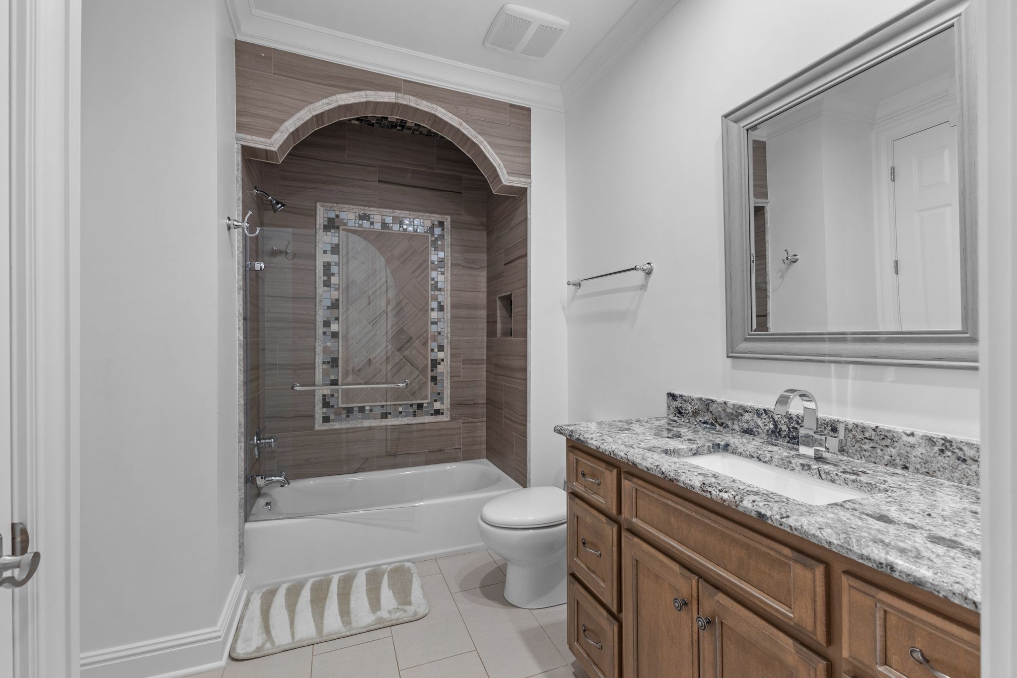Bathroom with an arched tiled tub surround, mosaic inset, and wood vanity with granite countertop.