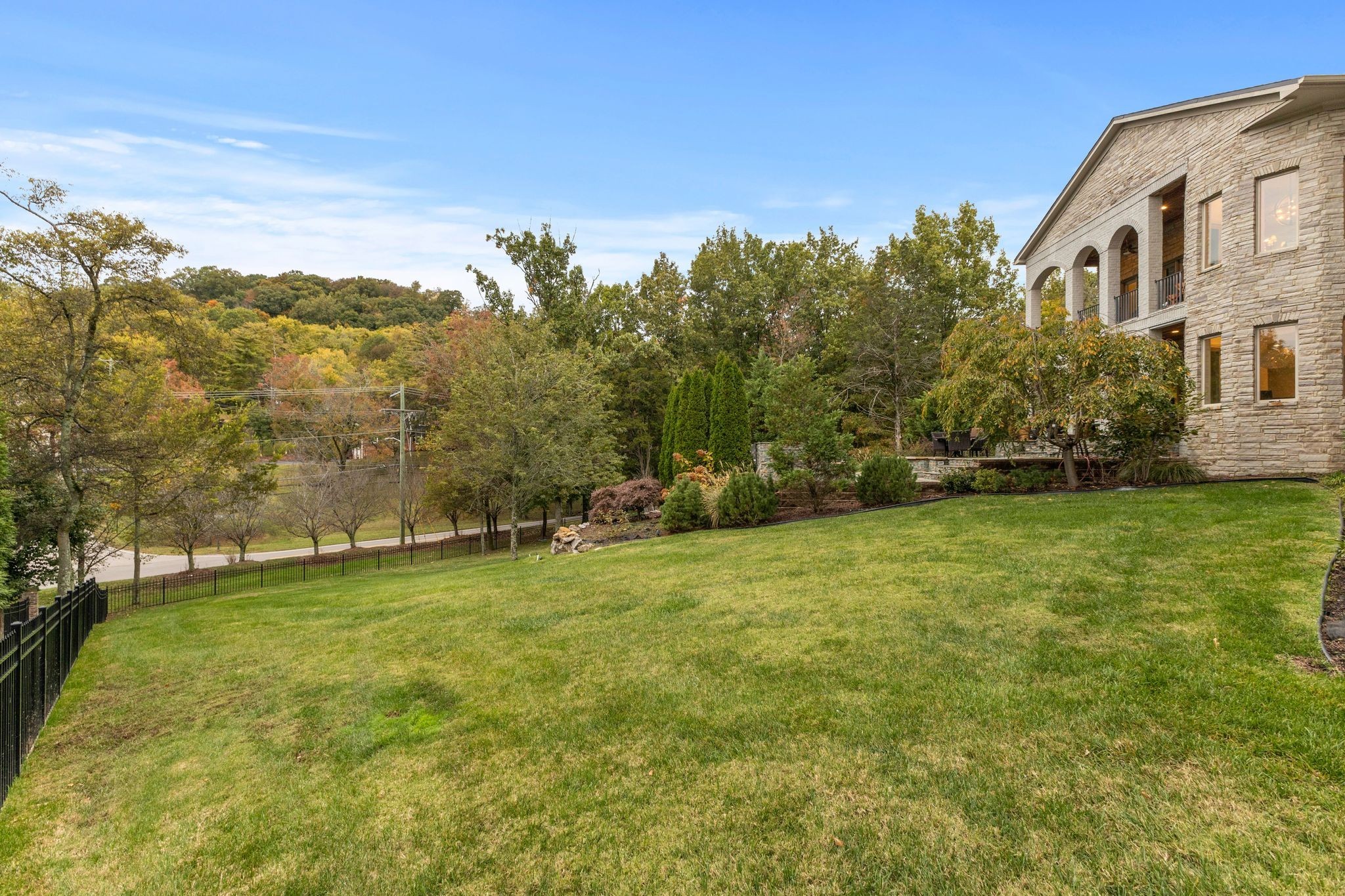 Stone house beside a sloping lawn, with arched balconies and wooded hills beyond.