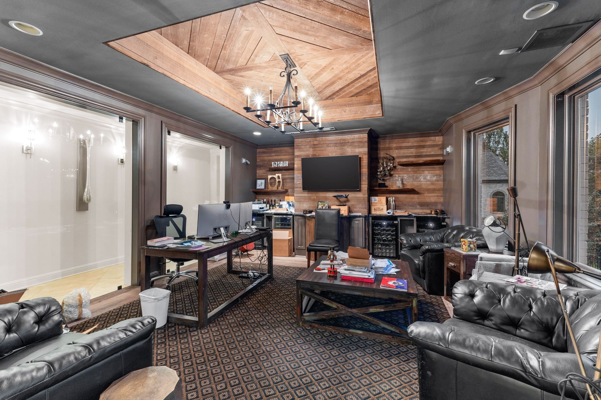 Home office and lounge with leather sofas, desks, a wood-paneled TV wall, and geometric wood ceiling.