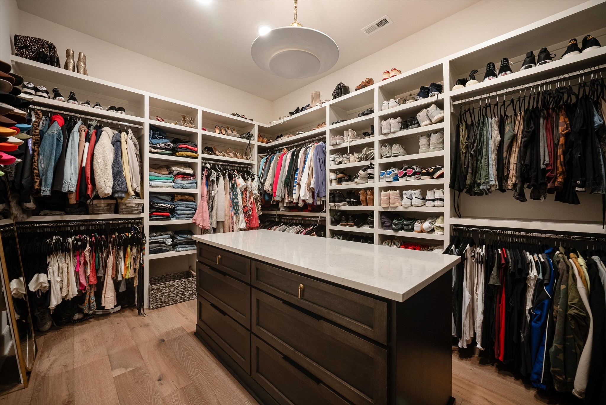 Walk-in closet with a central dark wood island, extensive shoe shelves, and clothes on hanging racks.