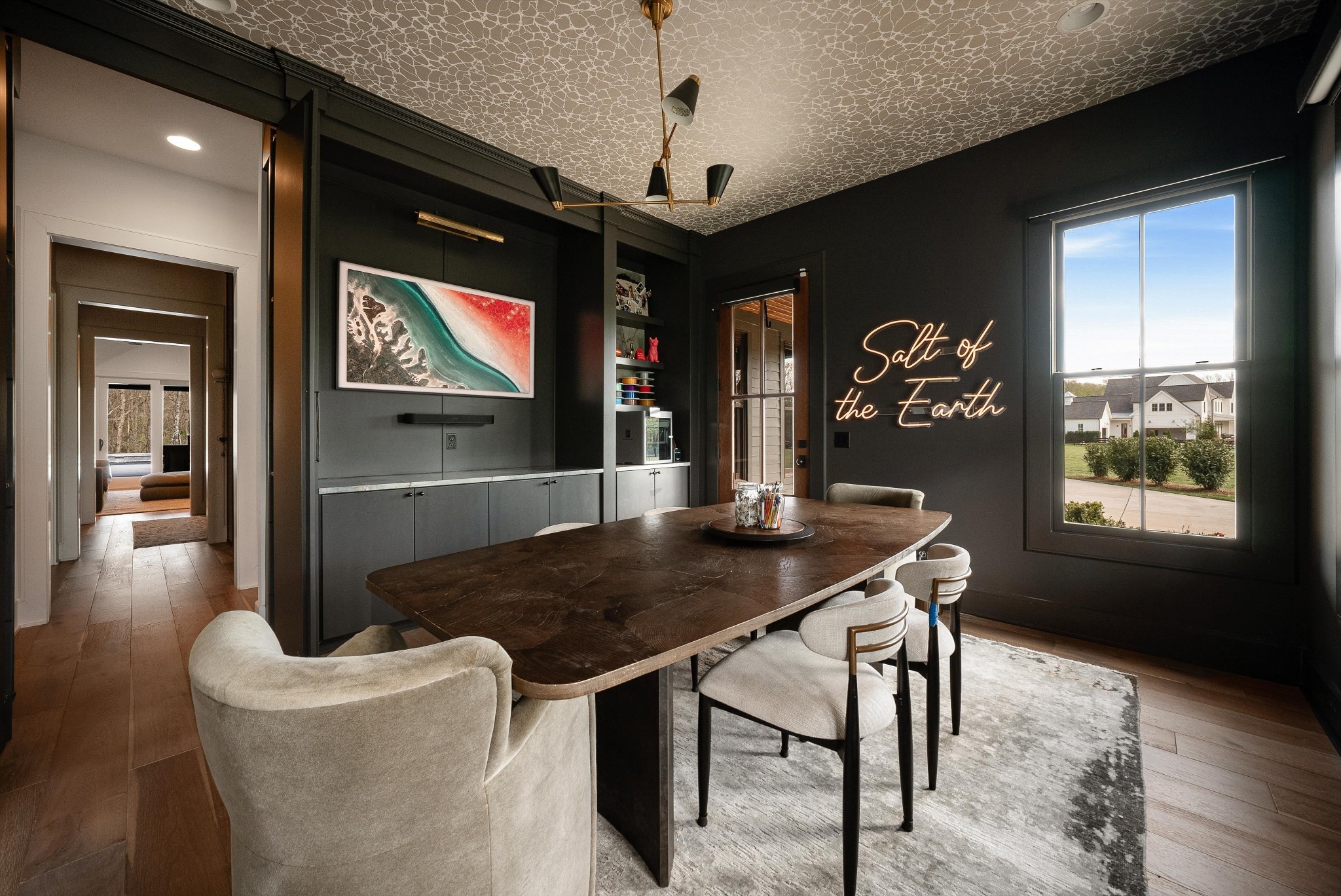 Dining room with a long dark wood table, built-in cabinets, and a lit “Salt of the Earth” sign.