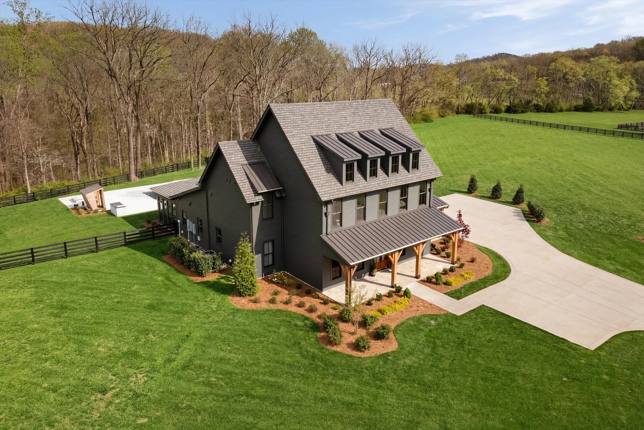 Aerial view of a dark gray home with dormers, a covered porch, and expansive green lawn.