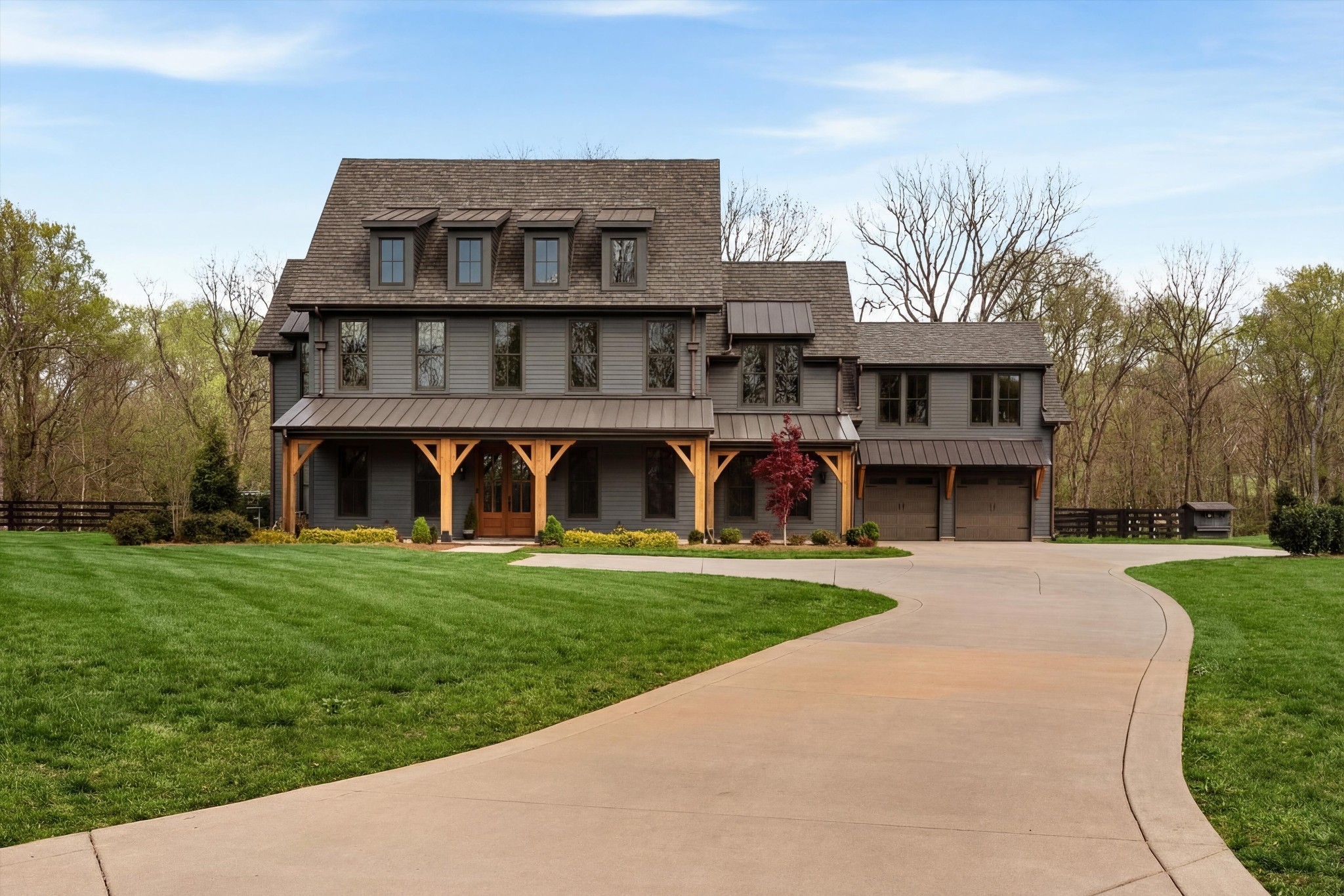 Gray two-story home with dormers, a timber porch, attached garage, and curved driveway.