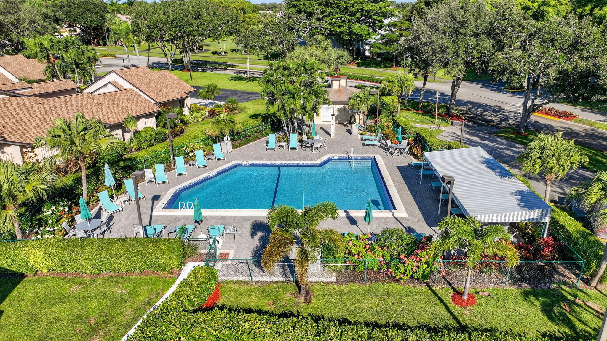 Community pool with turquoise water, lounge chairs, and a covered patio amid palm trees.