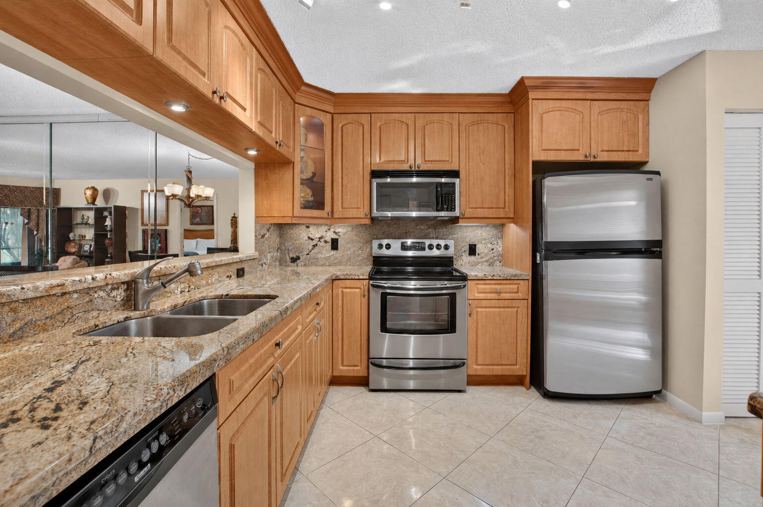 Kitchen with warm wood cabinets, patterned stone counters, stainless steel appliances, and a double-basin sink.