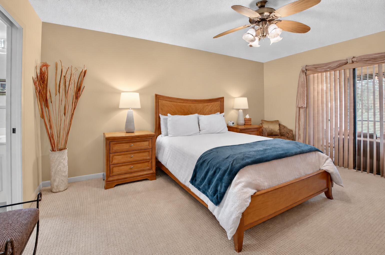 Bedroom with a wooden bed, blue throw, matching nightstands, and sliding glass door with vertical blinds.