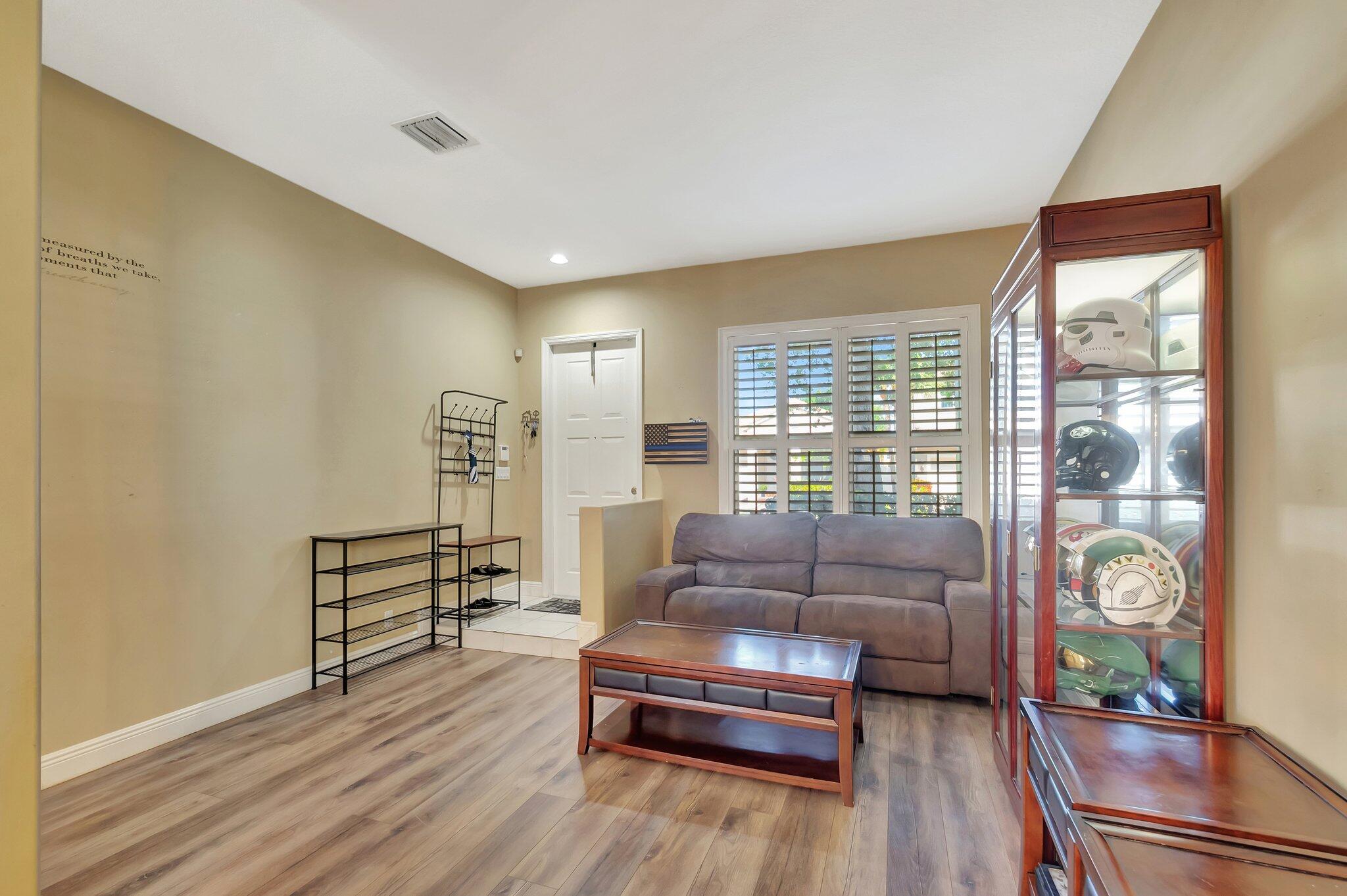 Living room with a gray sofa, plantation shutters, and a glass cabinet displaying helmets.