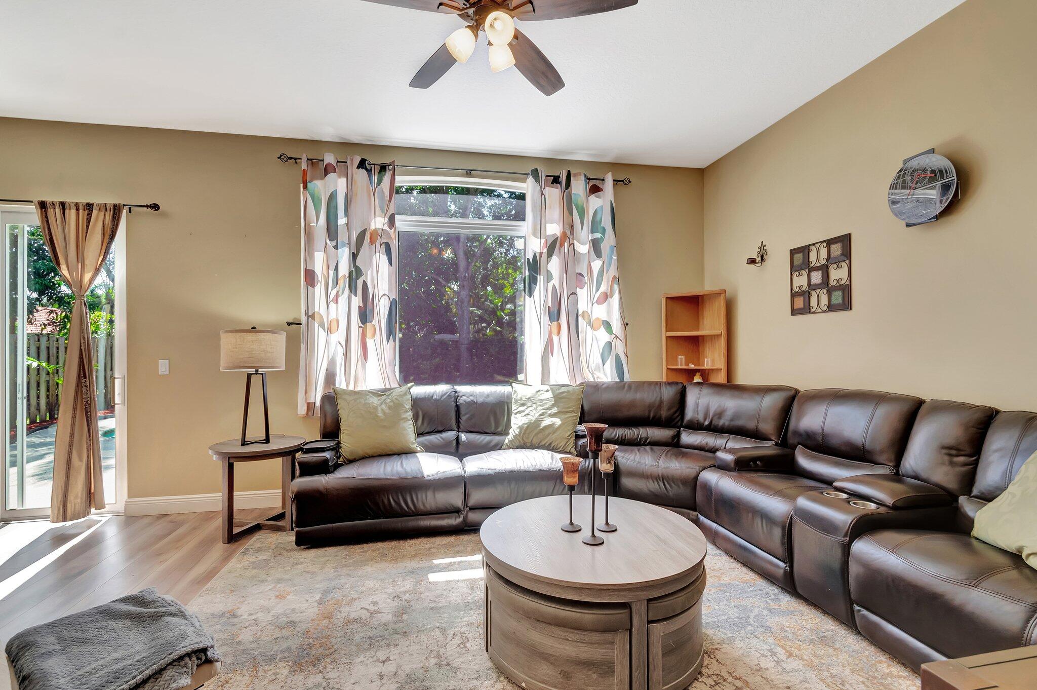 Living room with a dark leather sectional, round coffee table, and bright windows.
