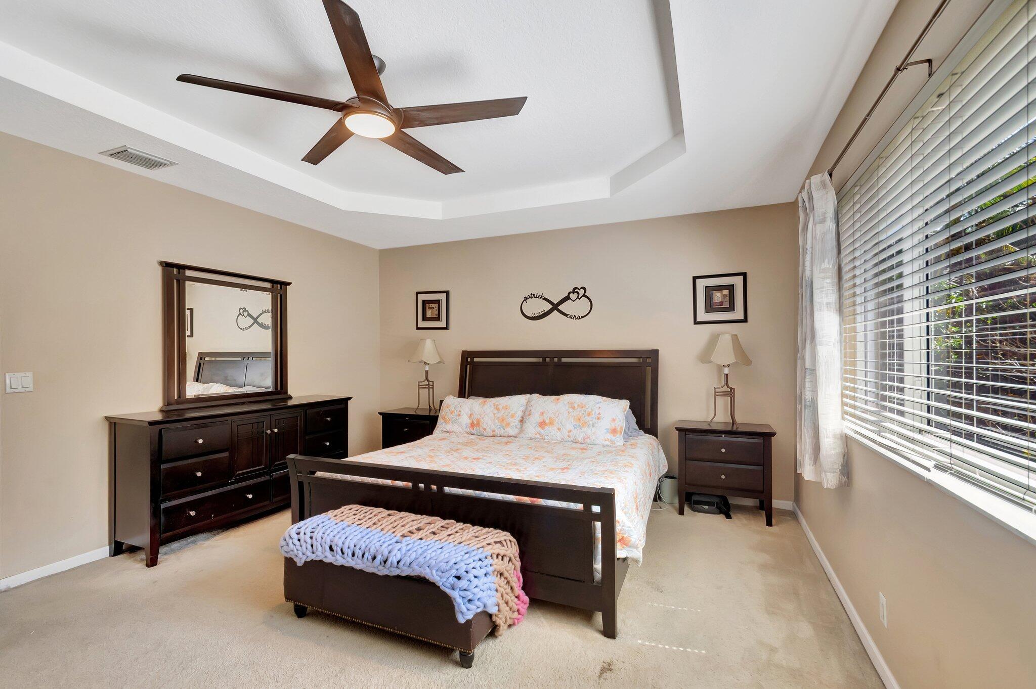 Furnished bedroom with dark wood furniture, floral bedding, a tray ceiling, and a large window.