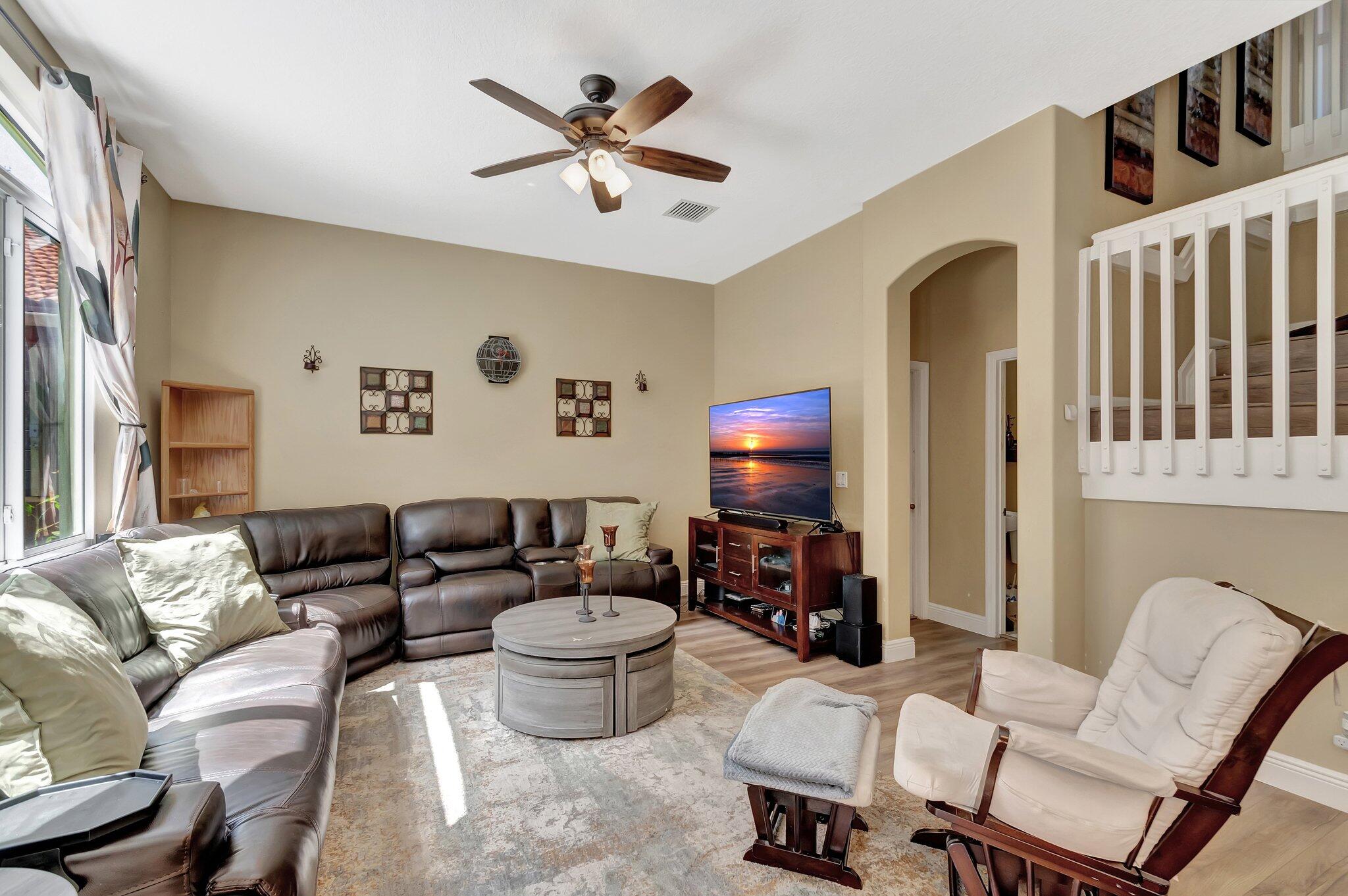 Furnished living room with a leather sectional, round coffee table, ceiling fan, and open staircase.