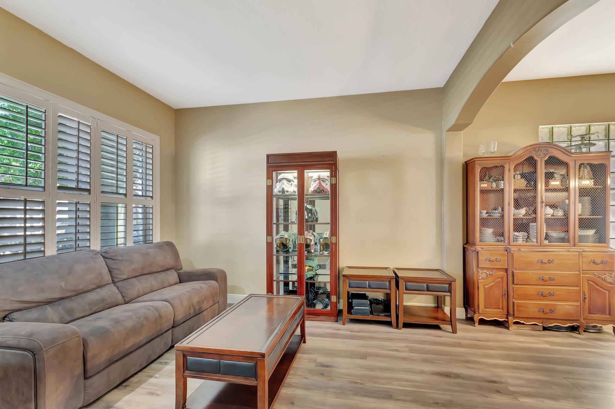 Living room with gray sectional, plantation shutters, and cabinets displaying collectibles.