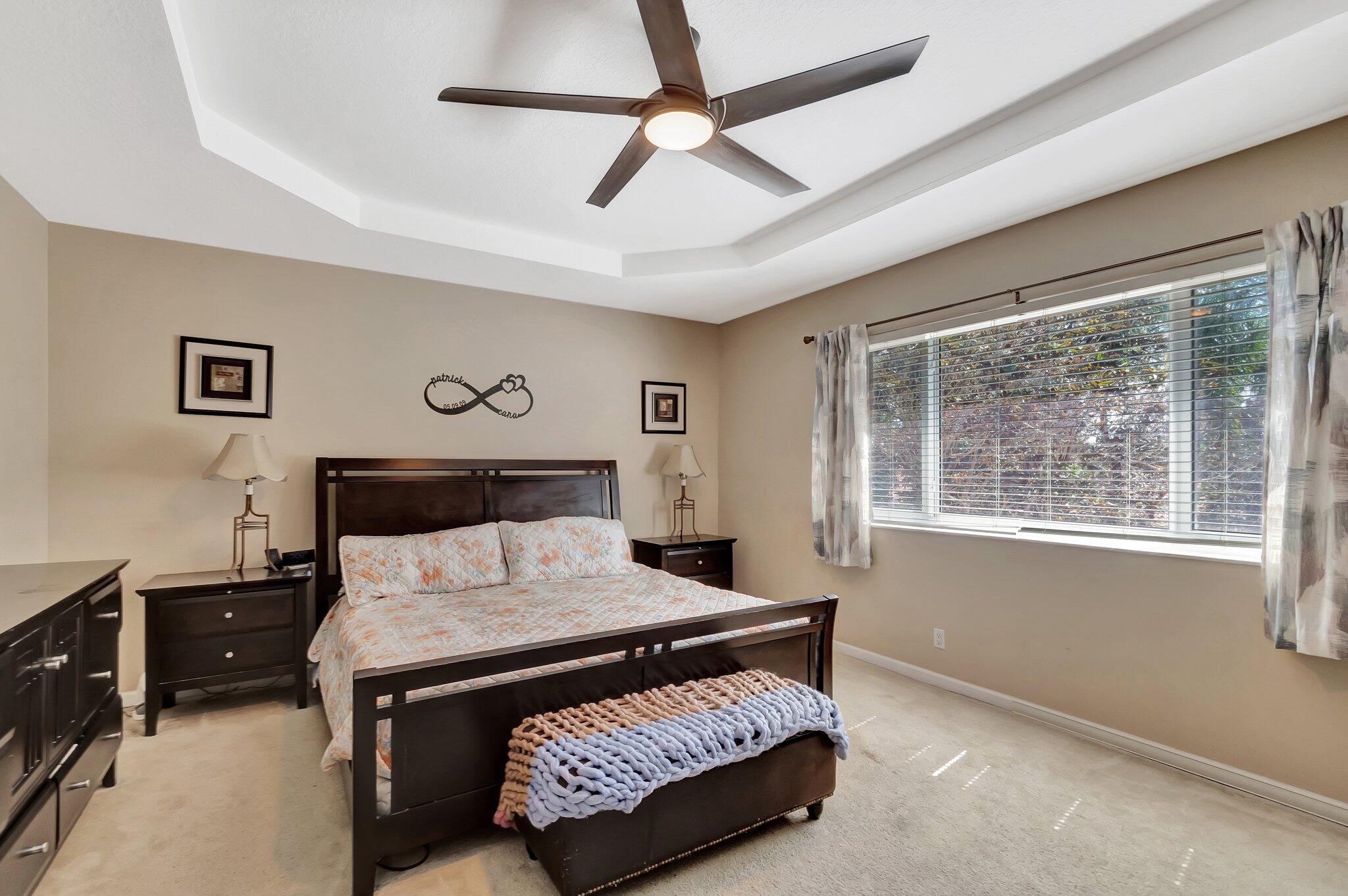 Bedroom with a dark wood bed, tray ceiling, ceiling fan, and large curtained window.
