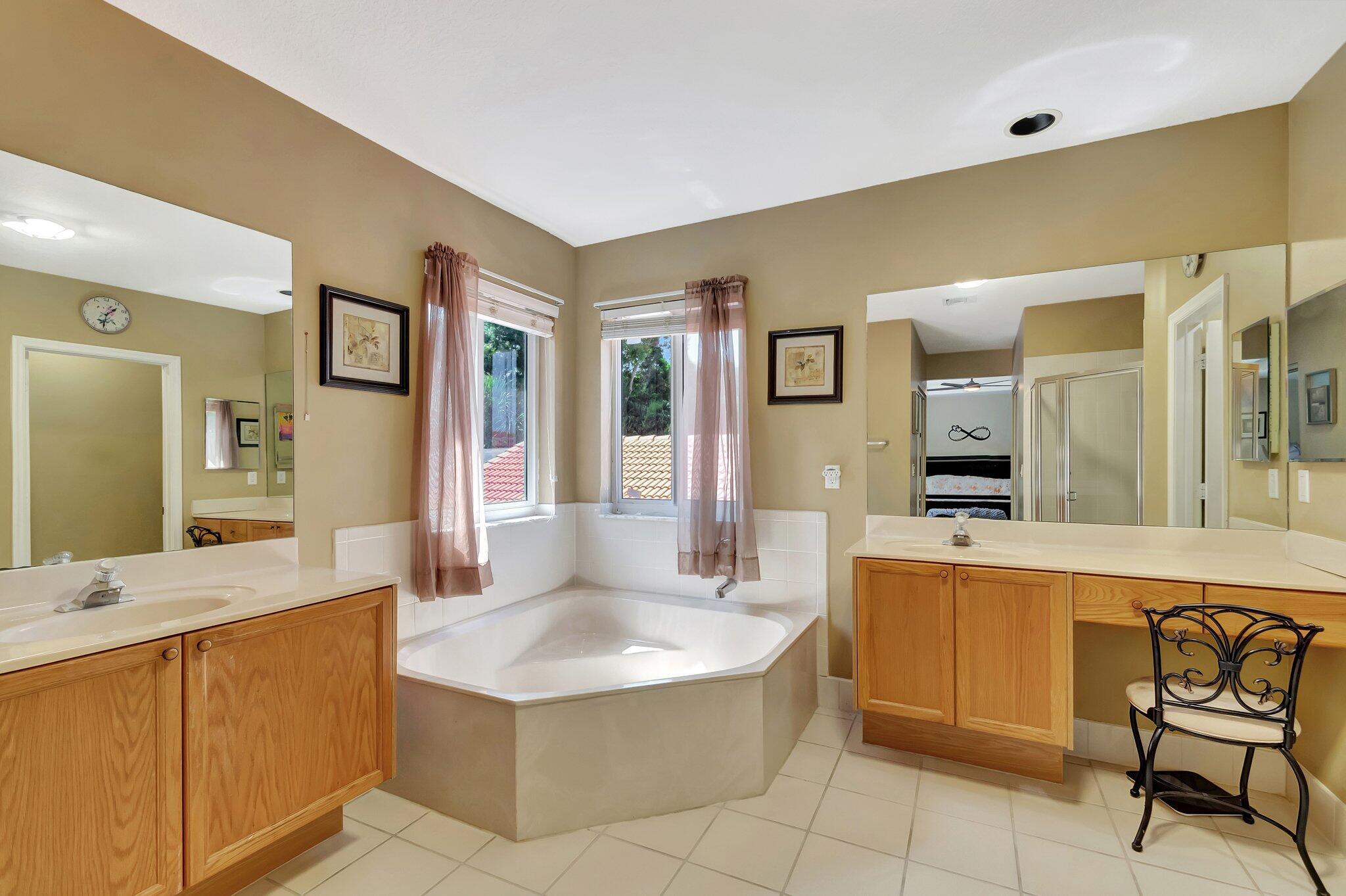 Bathroom with a corner soaking tub beneath two windows and wood double vanities.