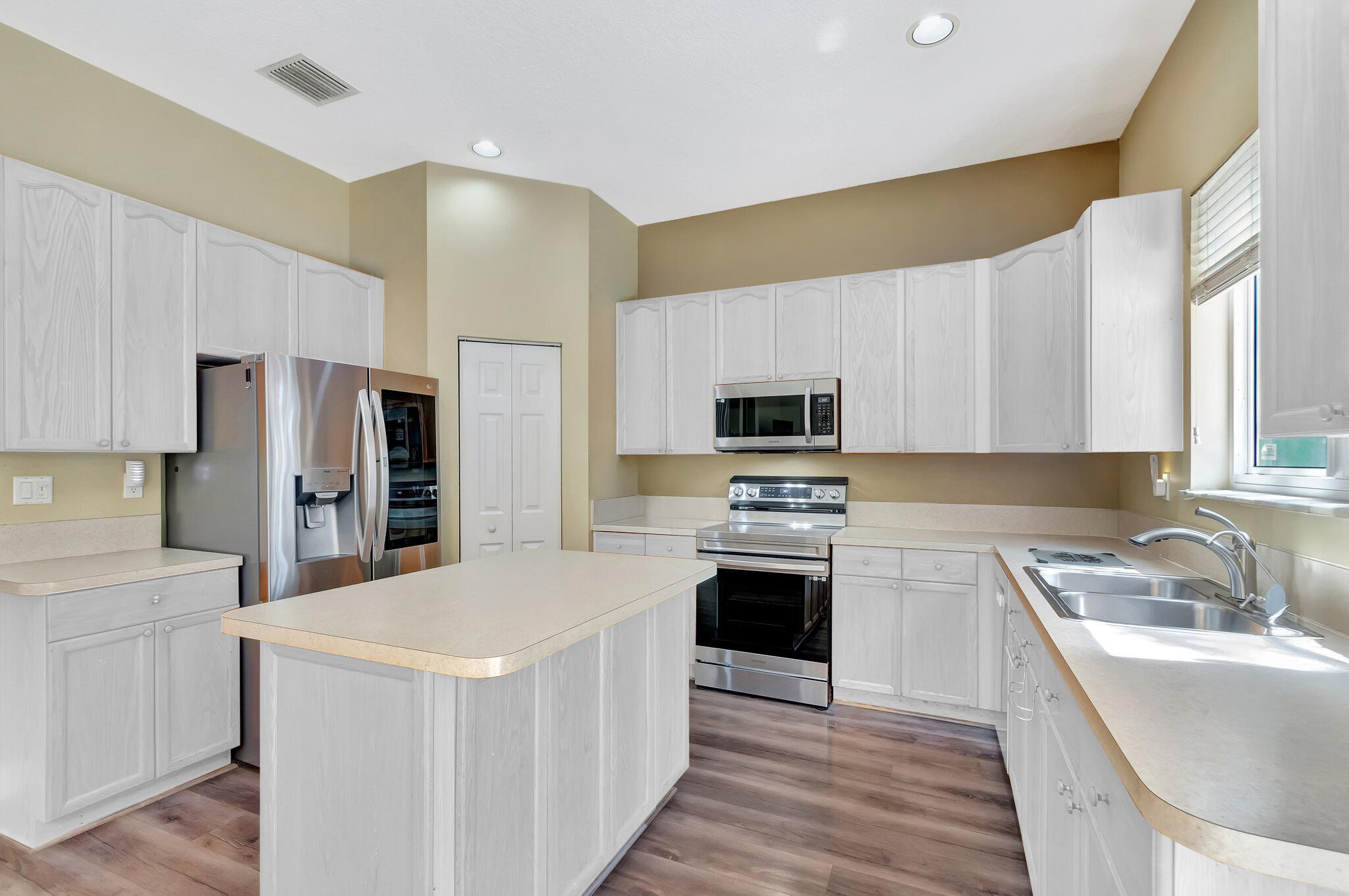 Kitchen with a large island, white cabinets, stainless steel appliances, and a double-basin sink.