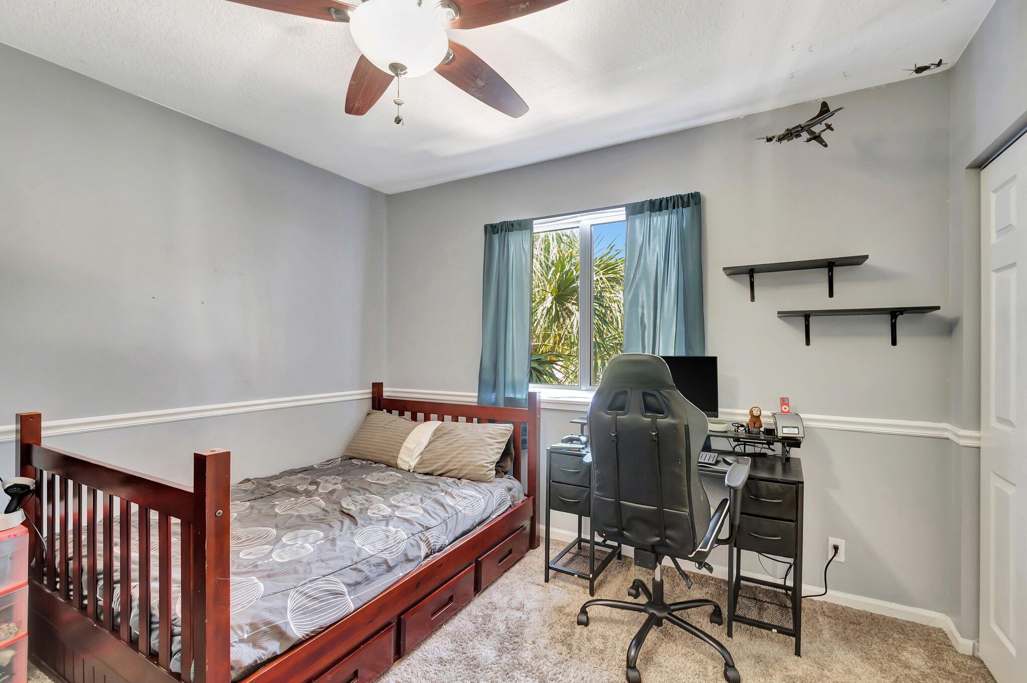 Bedroom with a dark wood bed, gaming desk and chair, blue curtains, and model airplanes on the wall.