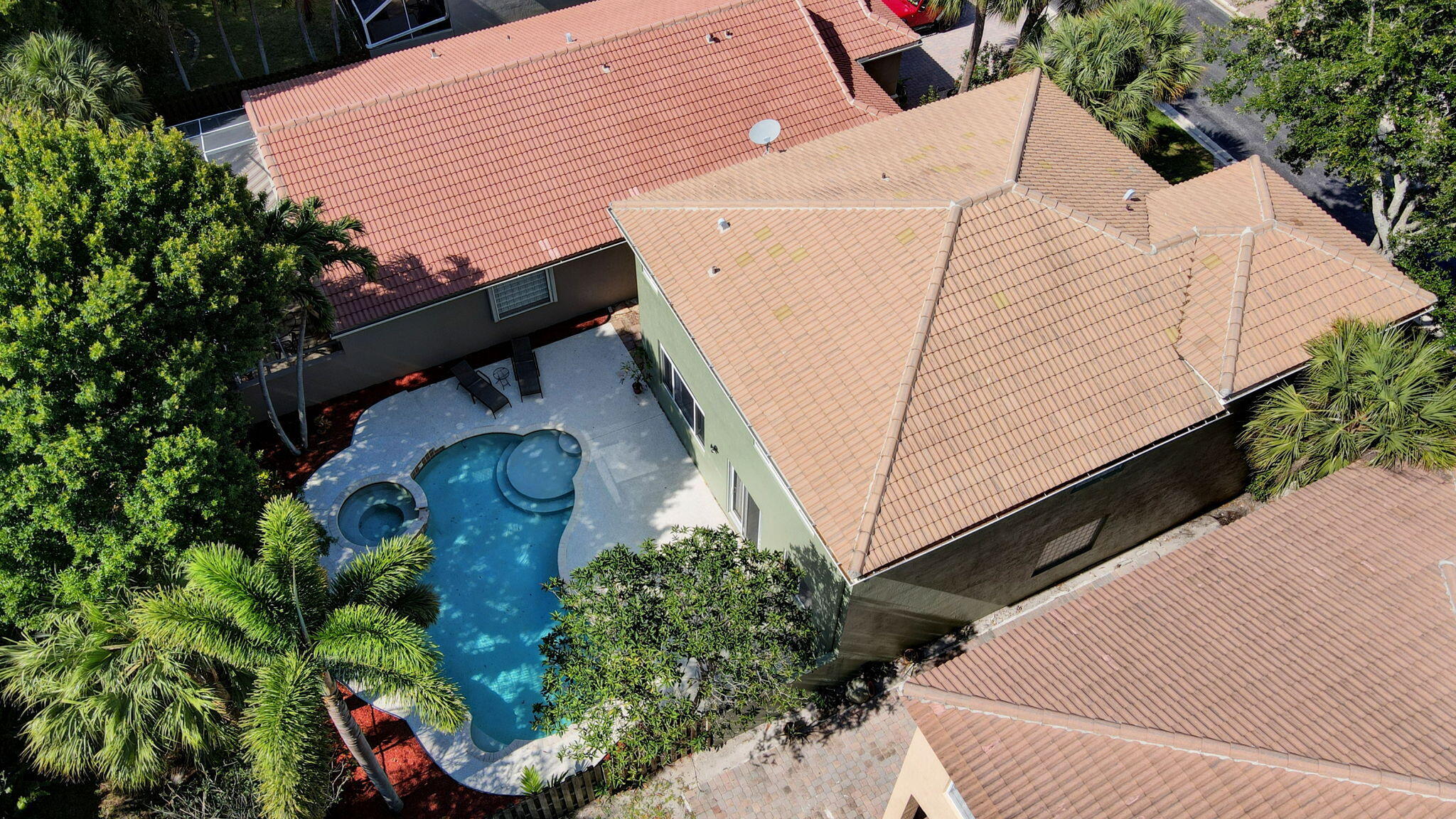 Aerial view of a tile-roofed home with a curved pool, attached spa, and tropical landscaping.
