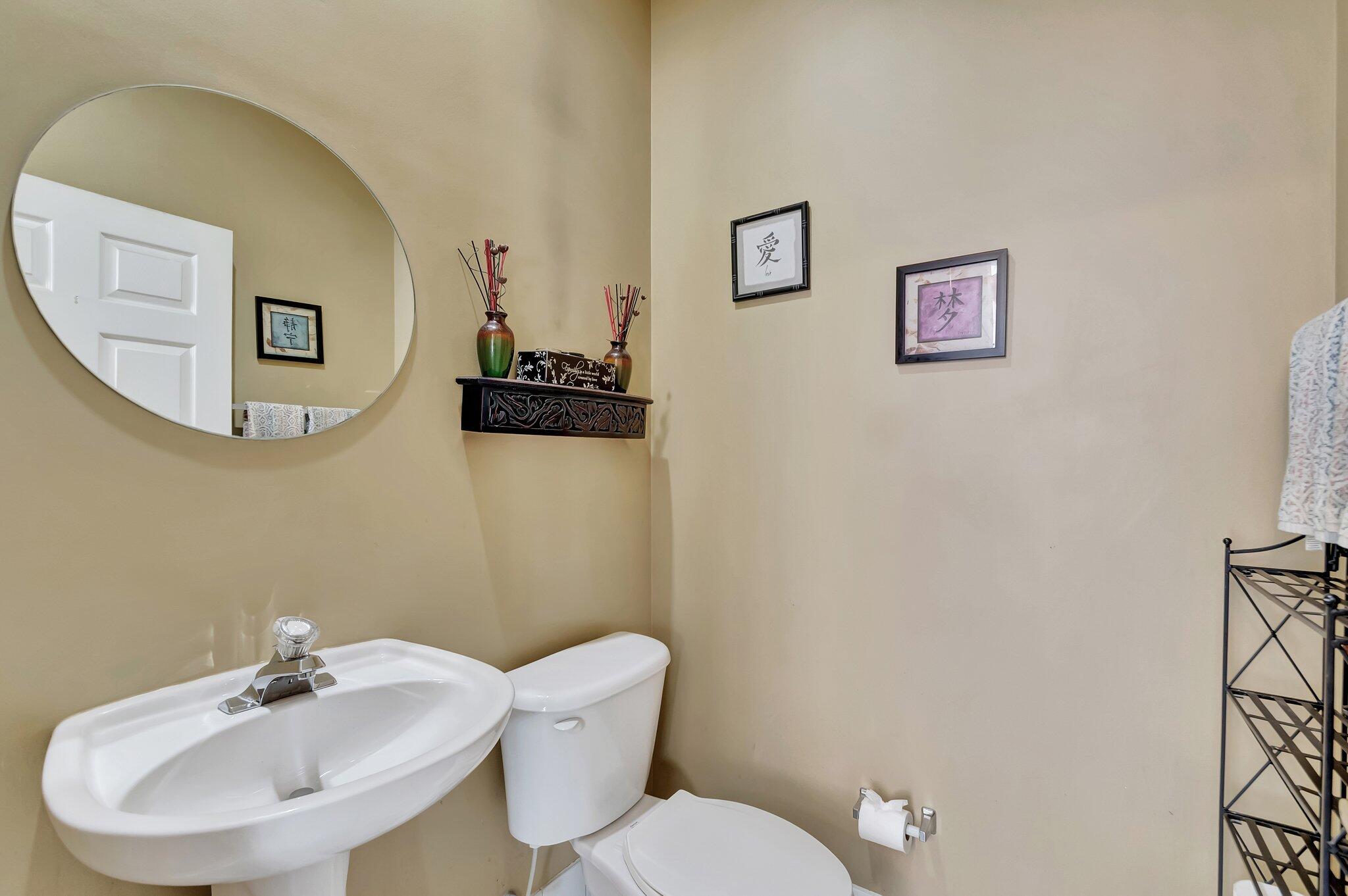 Bathroom with a white pedestal sink, toilet, large oval mirror, and decorative wall shelf.