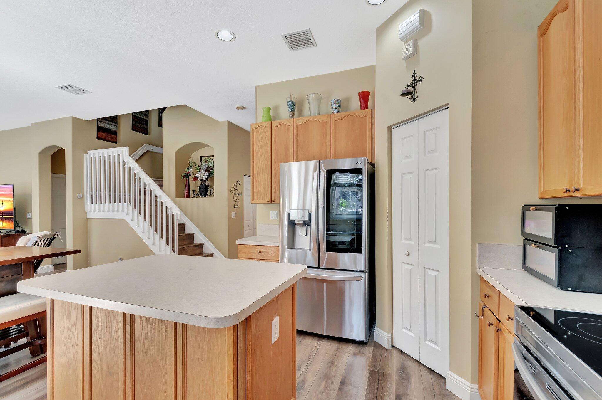 Kitchen with a large island, light wood cabinets, stainless steel appliances, and an adjoining staircase.