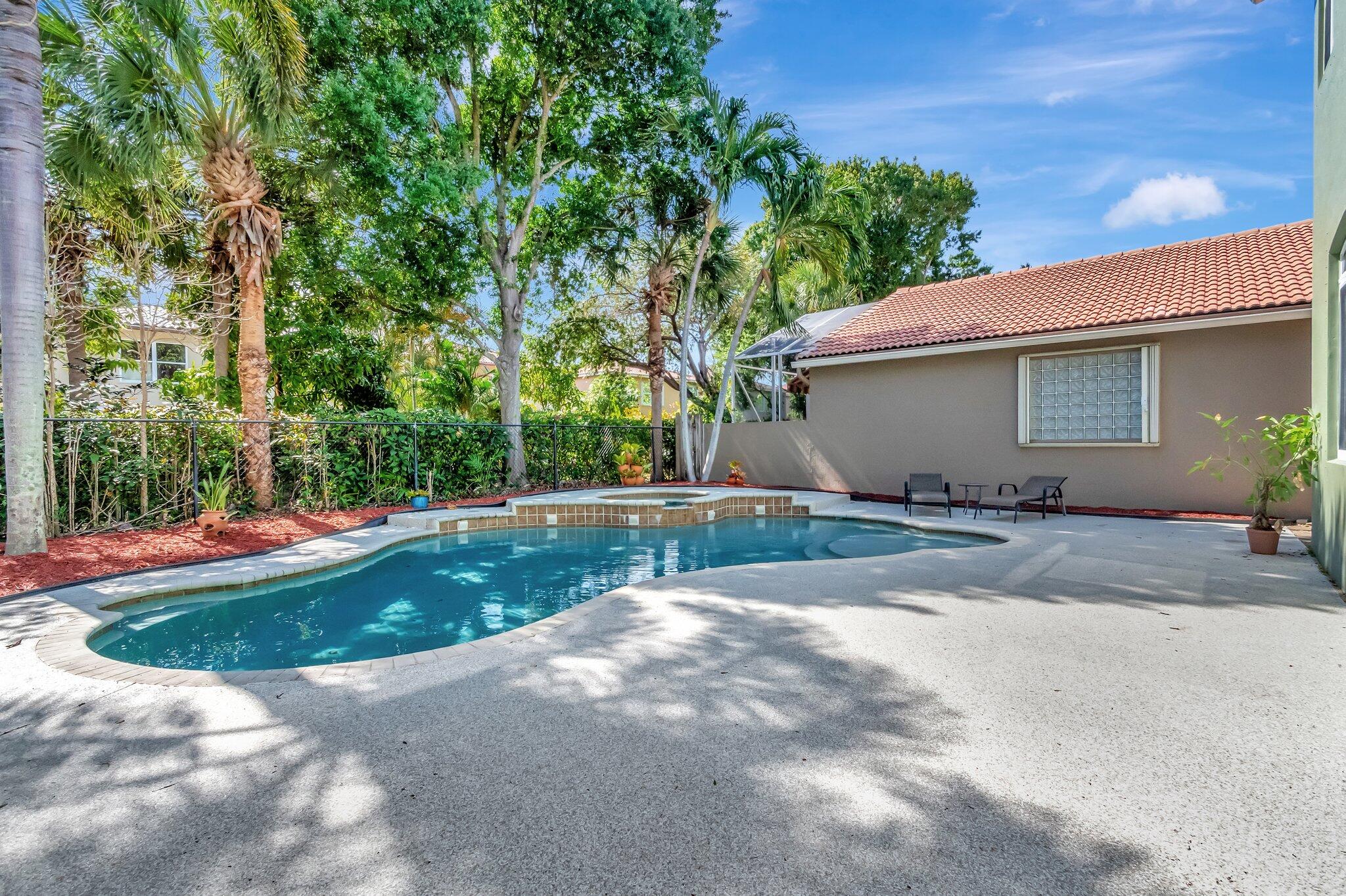Backyard pool and raised spa beside a concrete patio, tropical landscaping, and a terracotta-tile roof.
