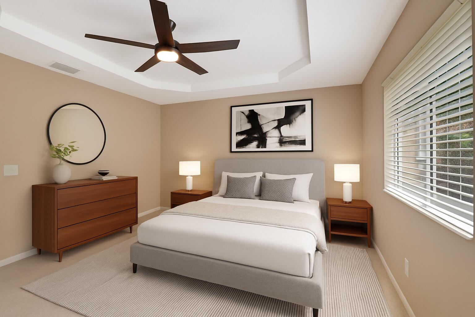 Furnished bedroom with a large bed, tray ceiling, dark ceiling fan, and wide window with white blinds.
