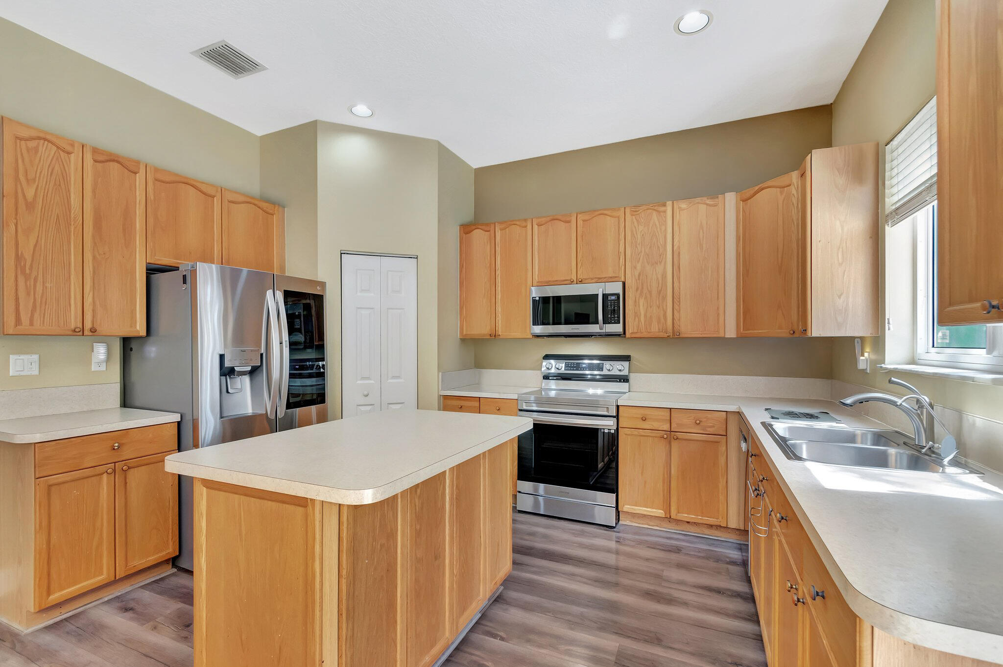 Kitchen with a large island, honey-colored cabinets, stainless steel appliances, and a double-basin sink.