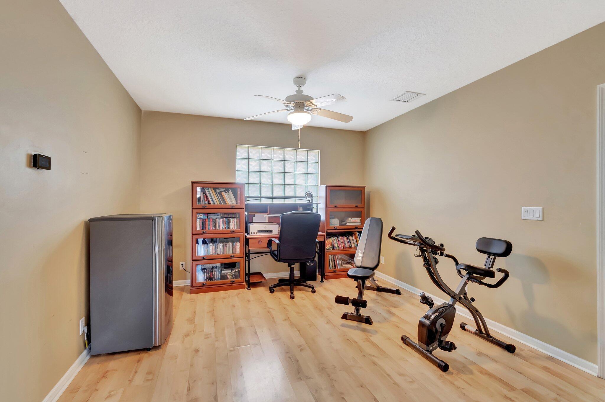 Home office and workout room with bookcases, glass-block window, stationary bike, and exercise bench.