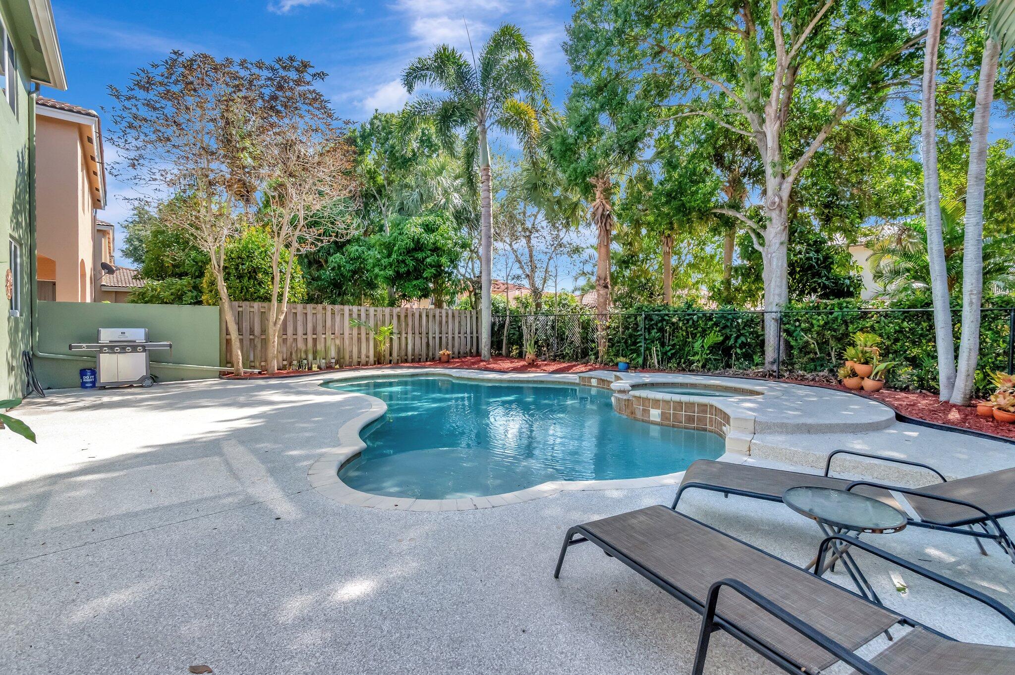 Backyard pool and raised spa with lounge chairs, a grill, and tropical landscaping.