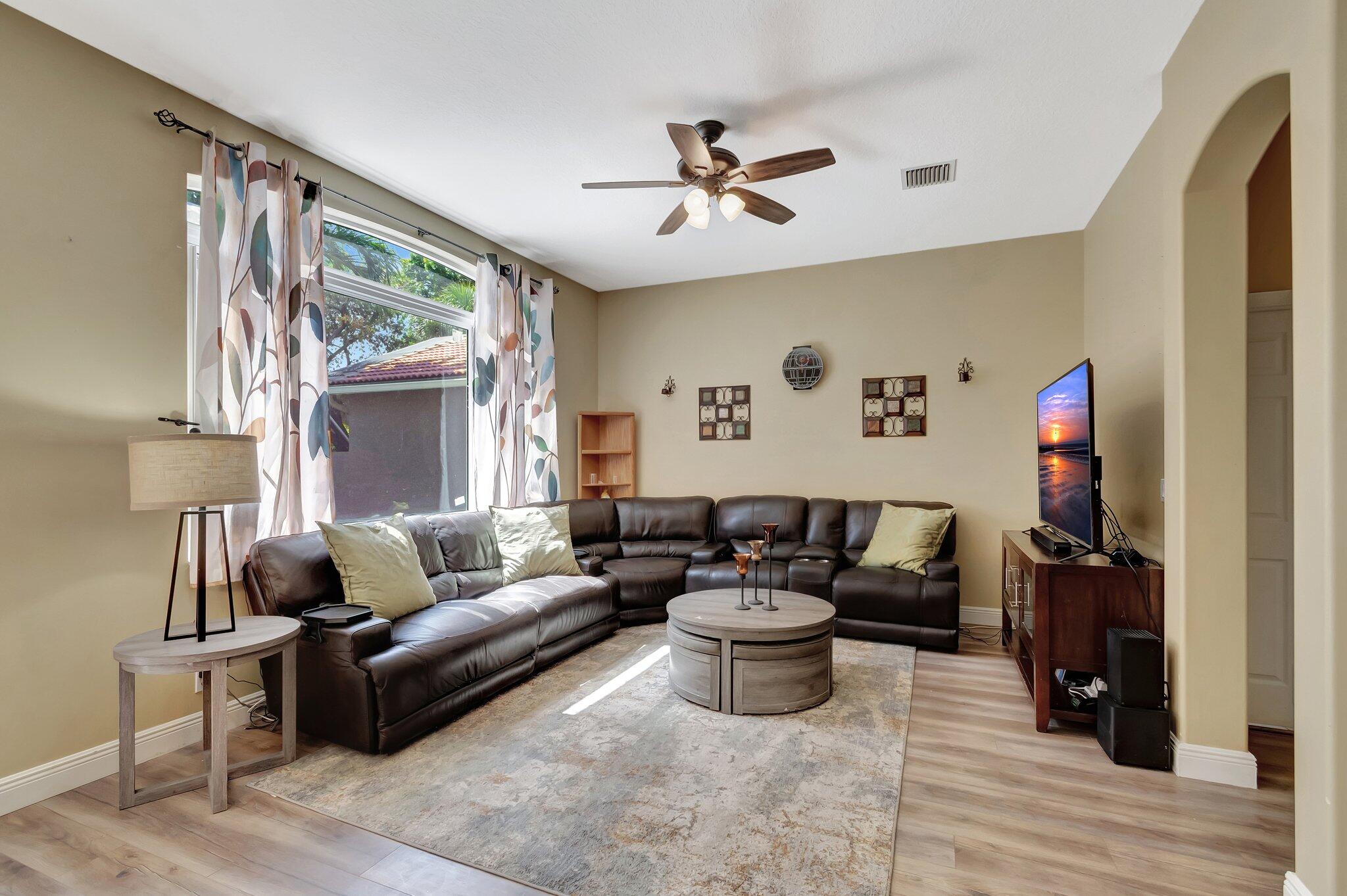 Living room with a dark leather sectional, round coffee table, and large curtained window.