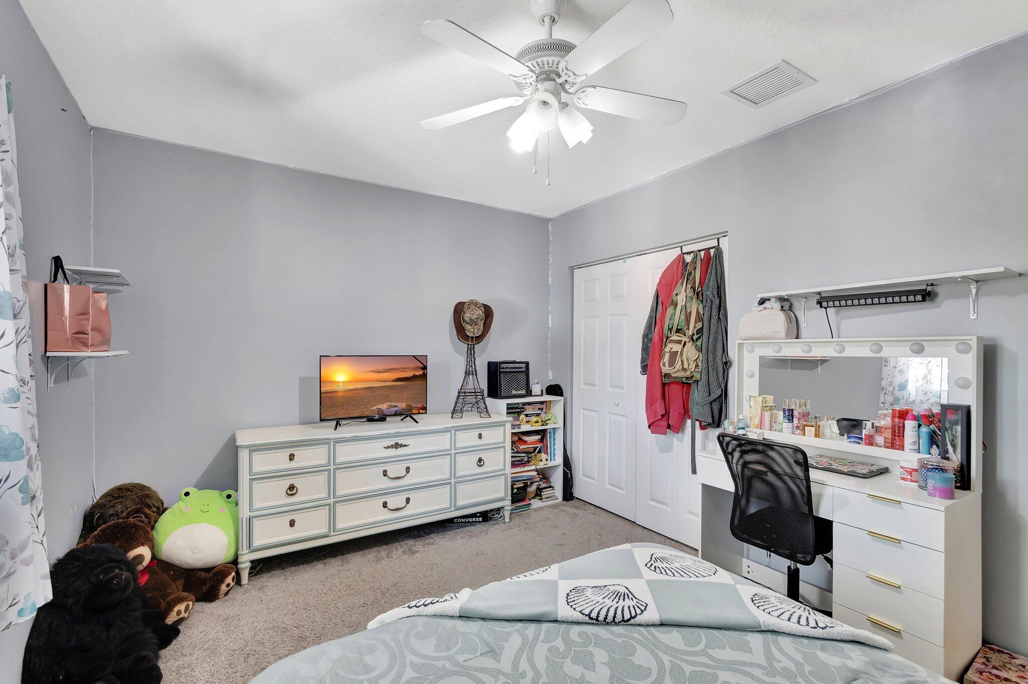 Bedroom with a makeup vanity, dresser and television, plush toys, and patterned bedding.