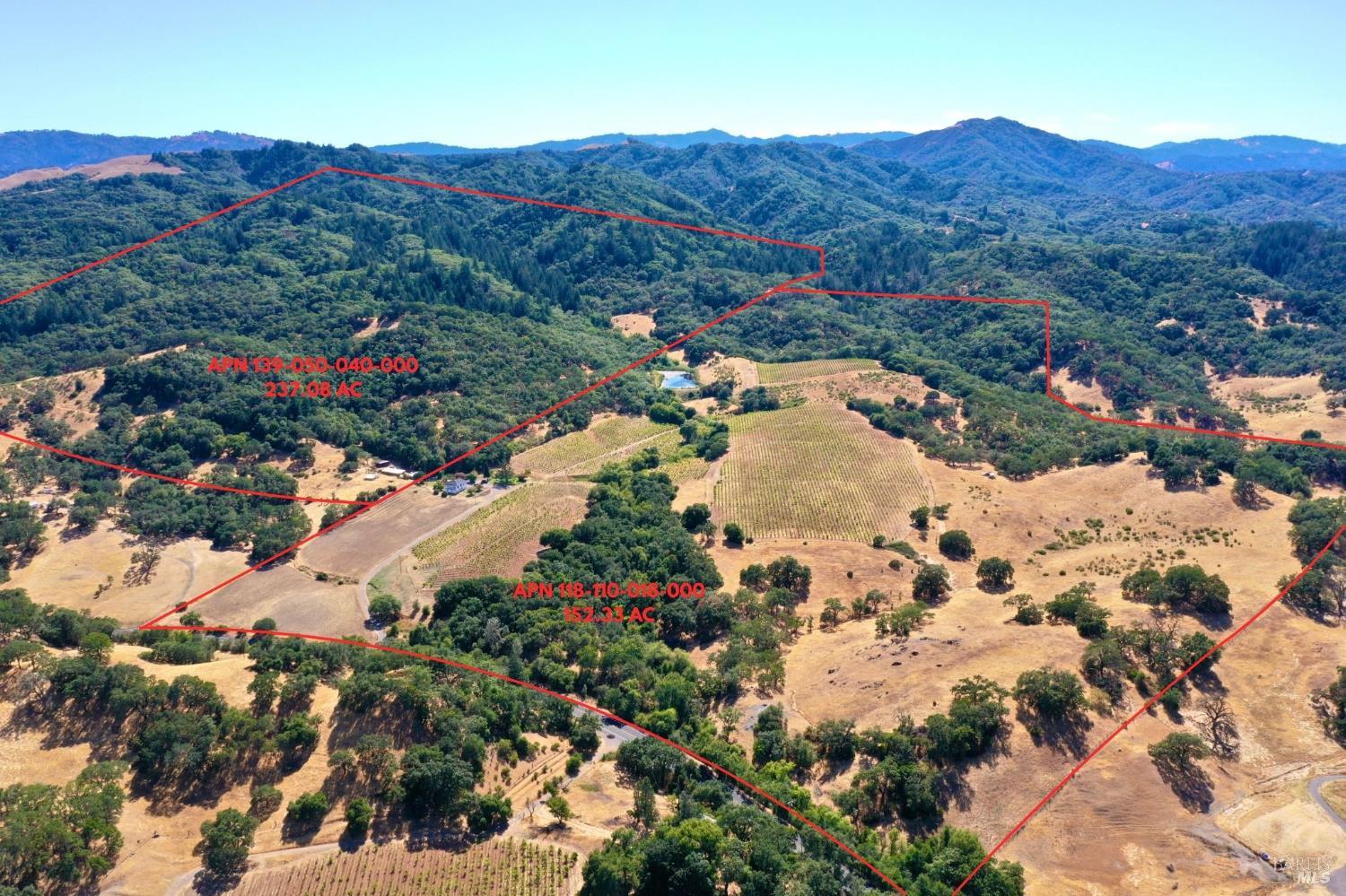Aerial view of wooded hills and vineyard acreage outlined in red, with distant mountain ridges.