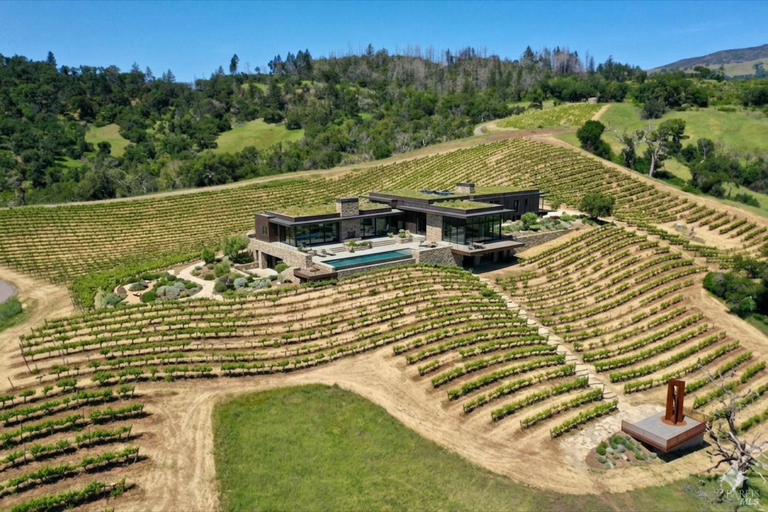 Modern home and swimming pool surrounded by vineyard rows on rolling hills.