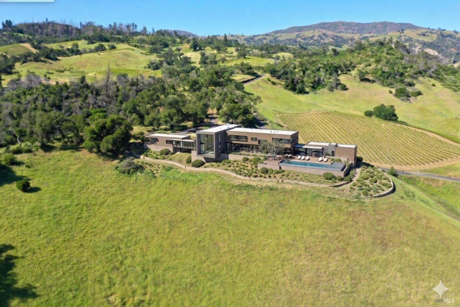 Modern home and swimming pool amid vineyard rows and rolling hills.