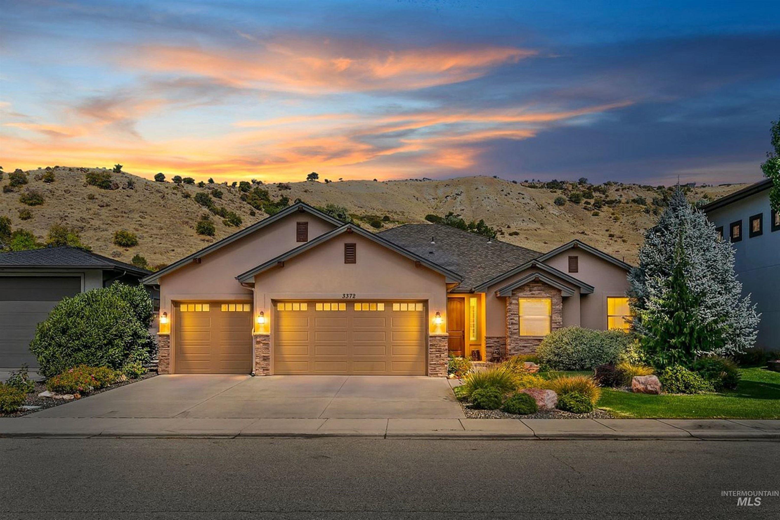 Single-story home with a three-car garage, landscaped front yard, and rolling hills behind it at dusk.