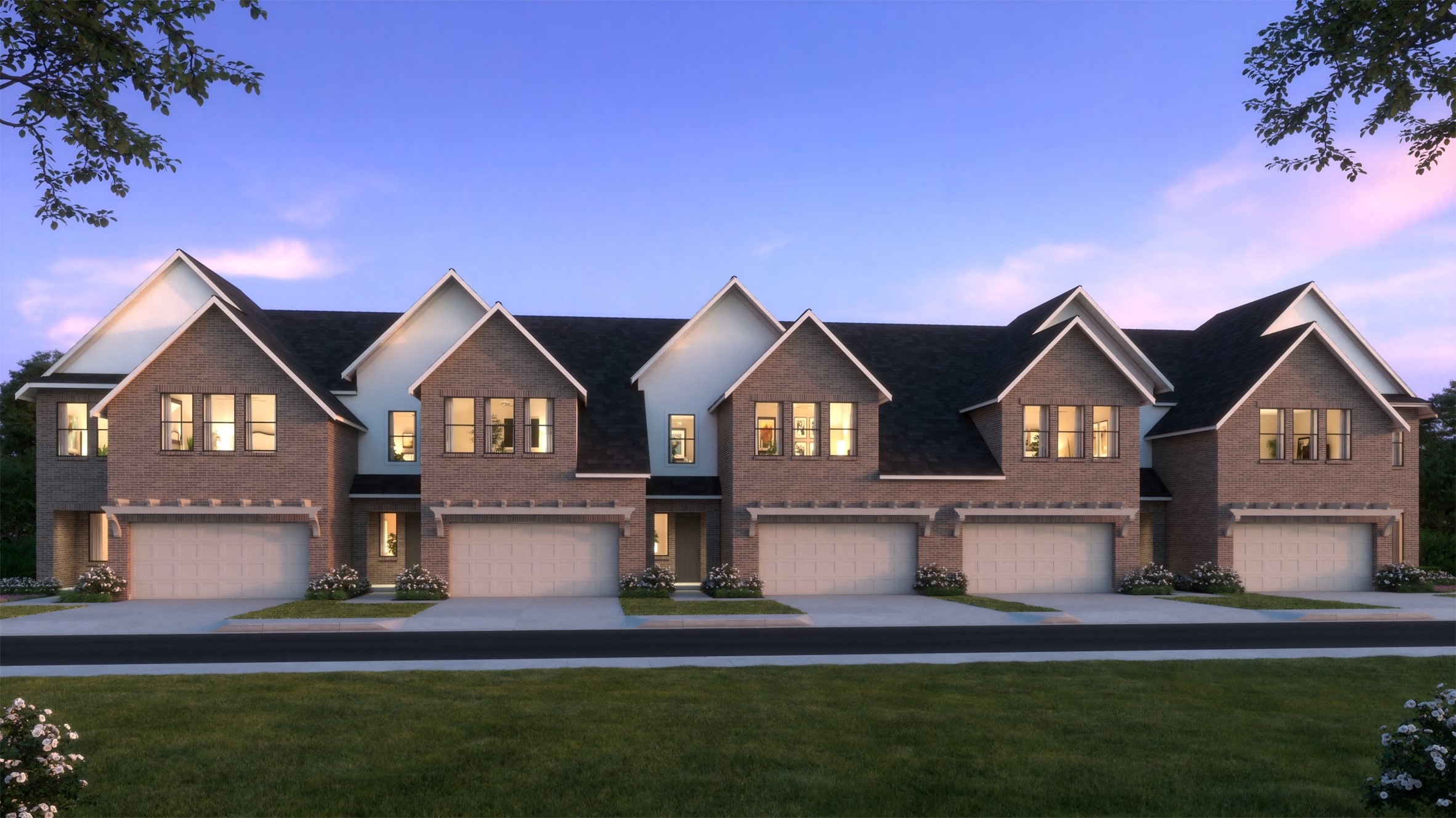 Attached brick townhomes with front garages and lit windows at dusk.