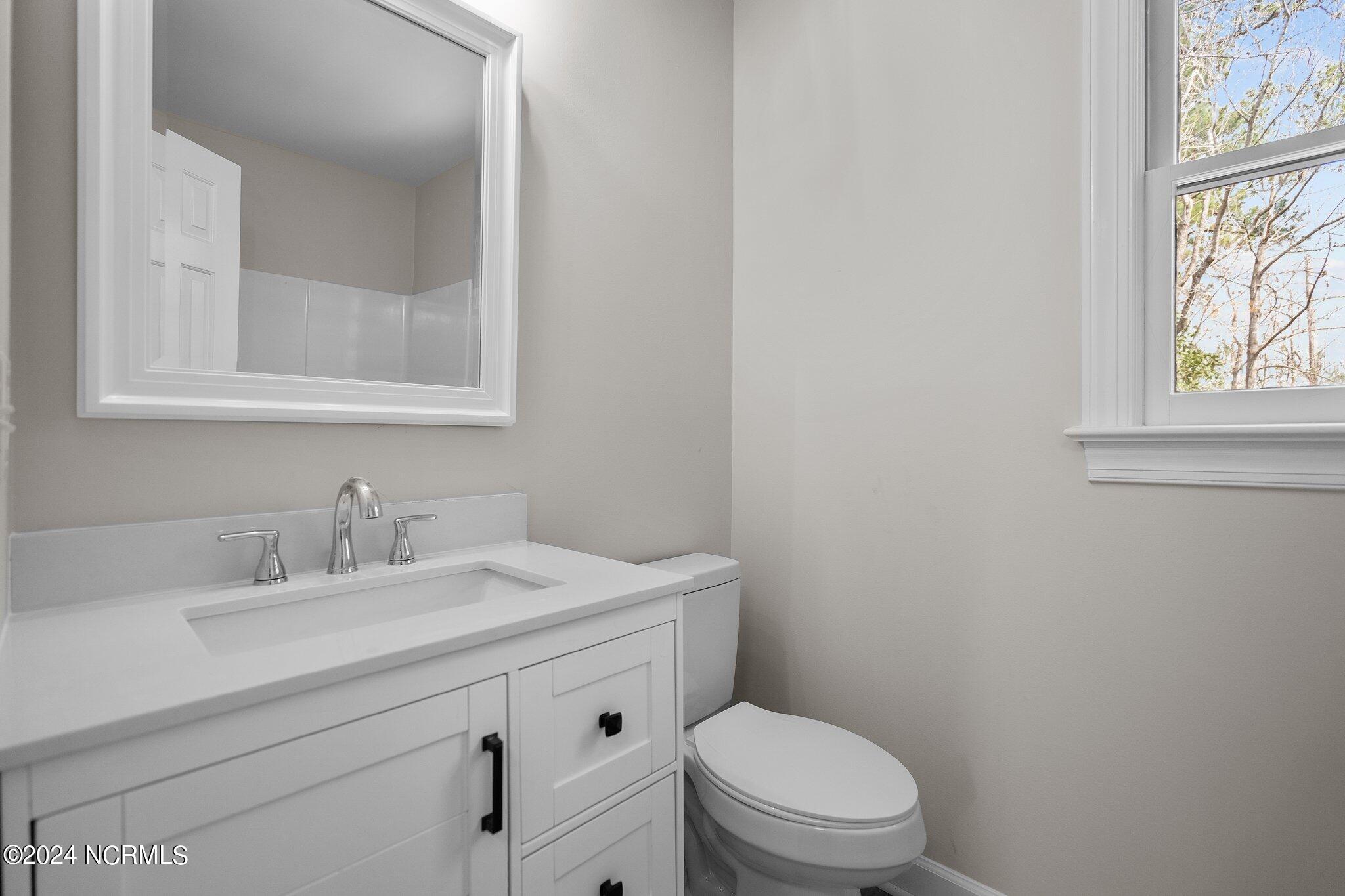 Bathroom with a white vanity and toilet beside a window overlooking leafless trees.