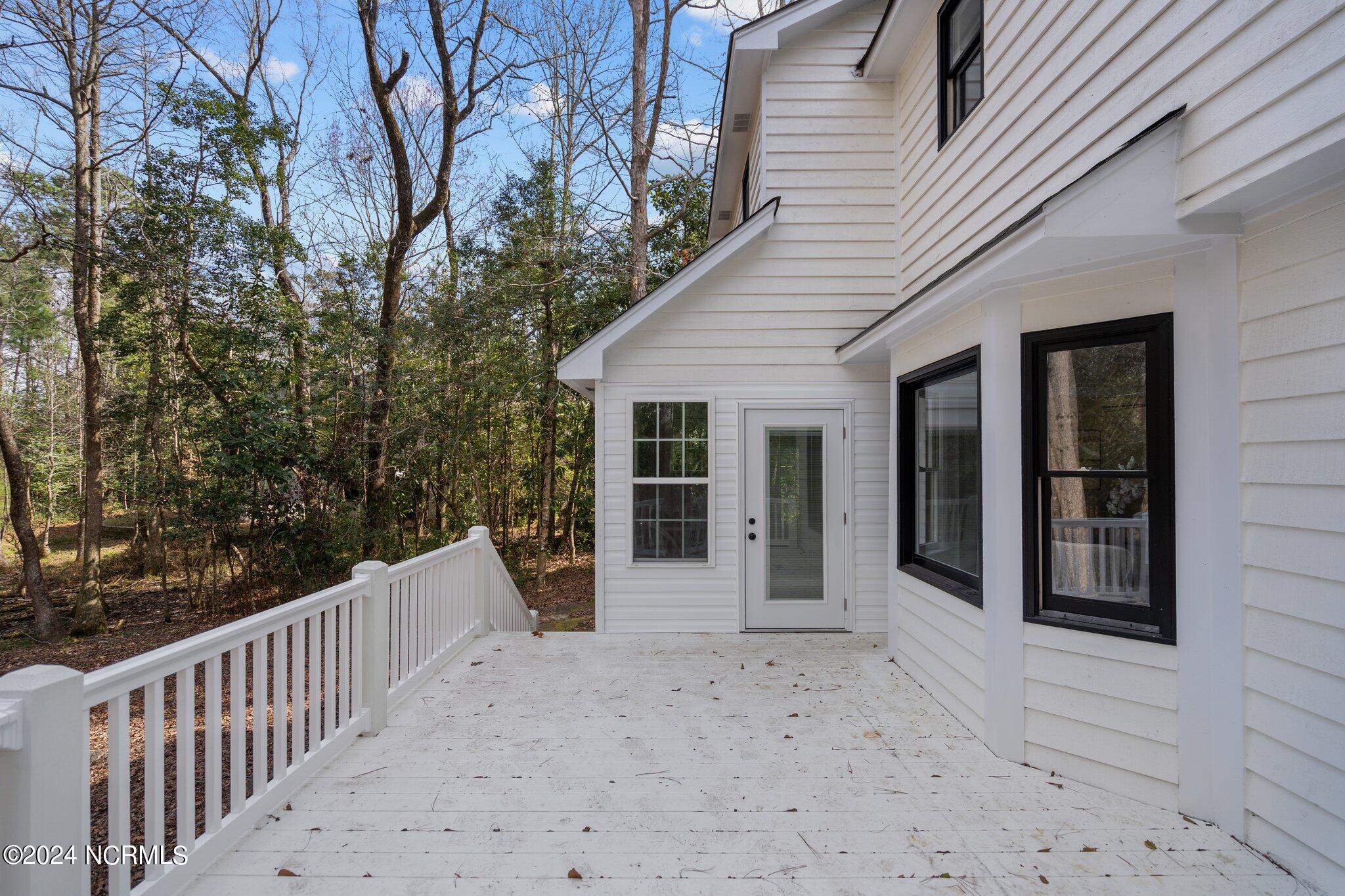 White rear deck beside a white-sided house, overlooking trees.