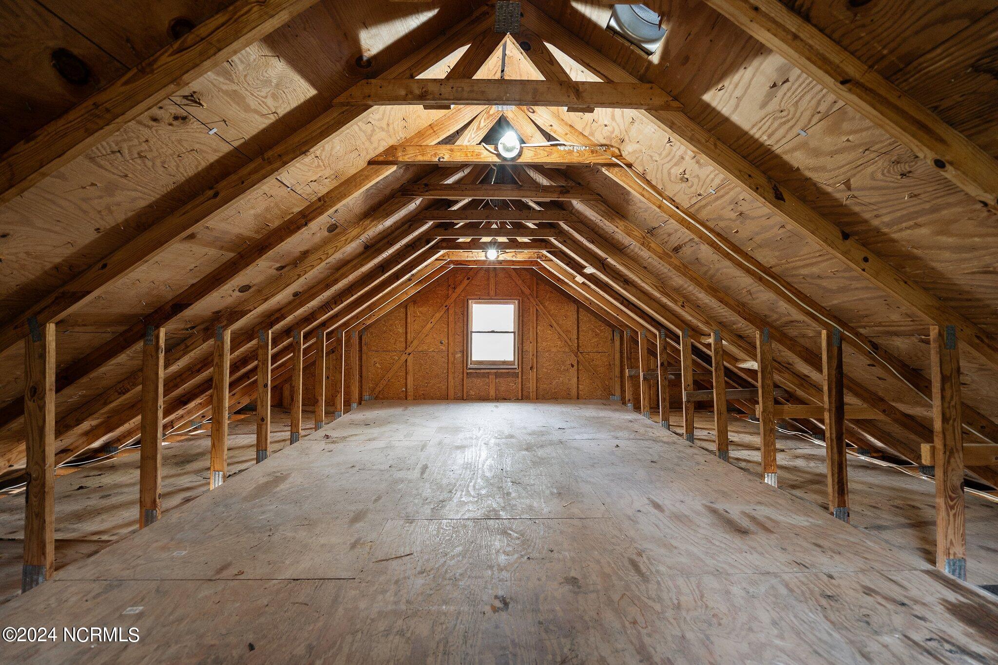 Unfinished attic with exposed wooden roof trusses and a plywood floor.