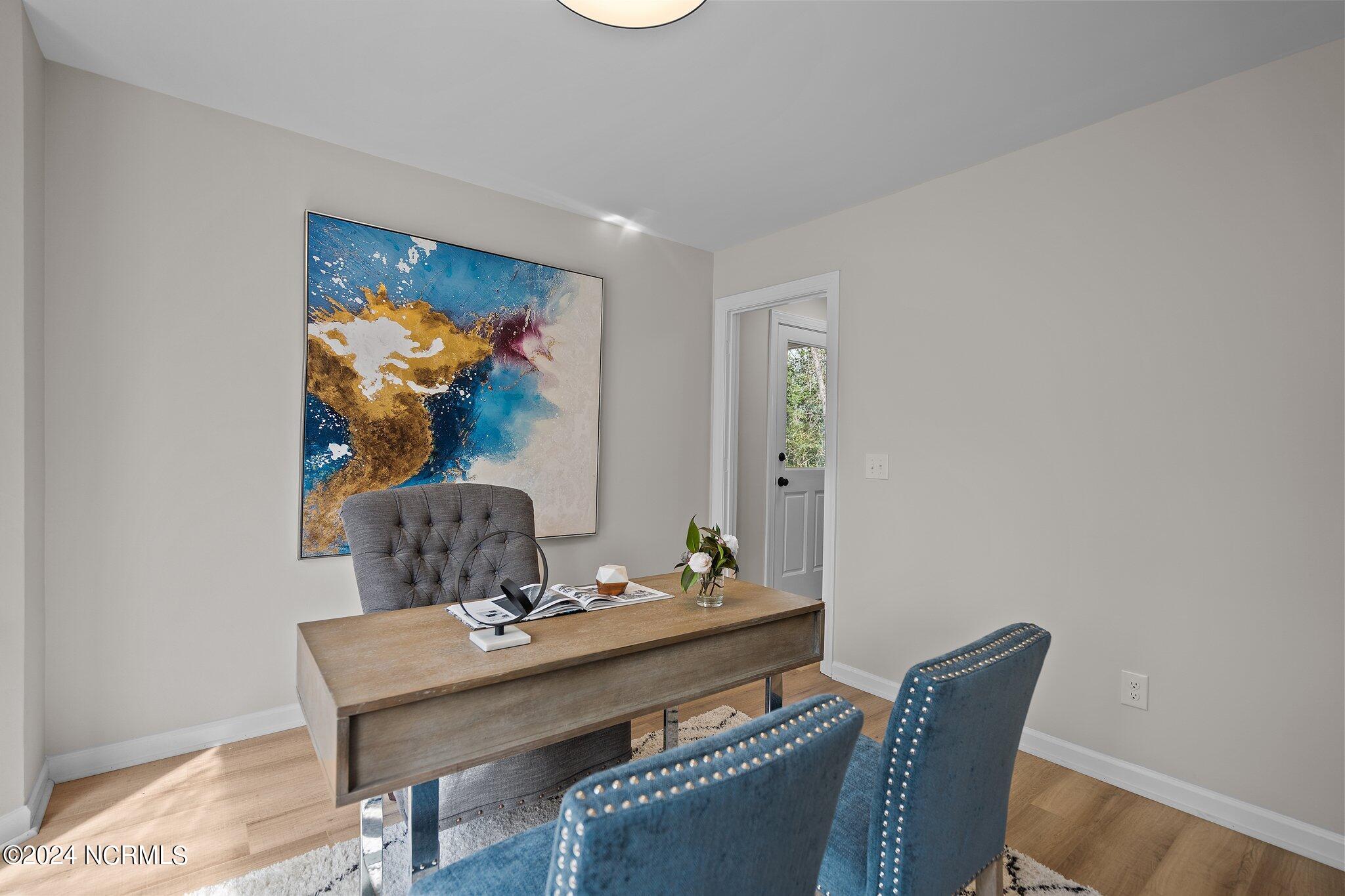 Staged home office with a wooden desk, blue chairs, and large abstract wall art.