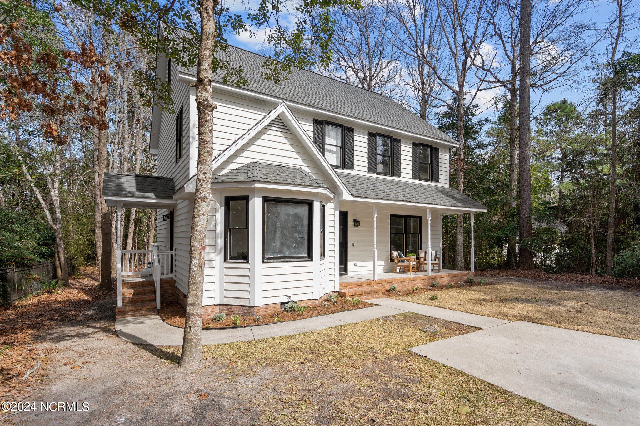 Two-story white house with a bay window, covered porch, and wooded yard.