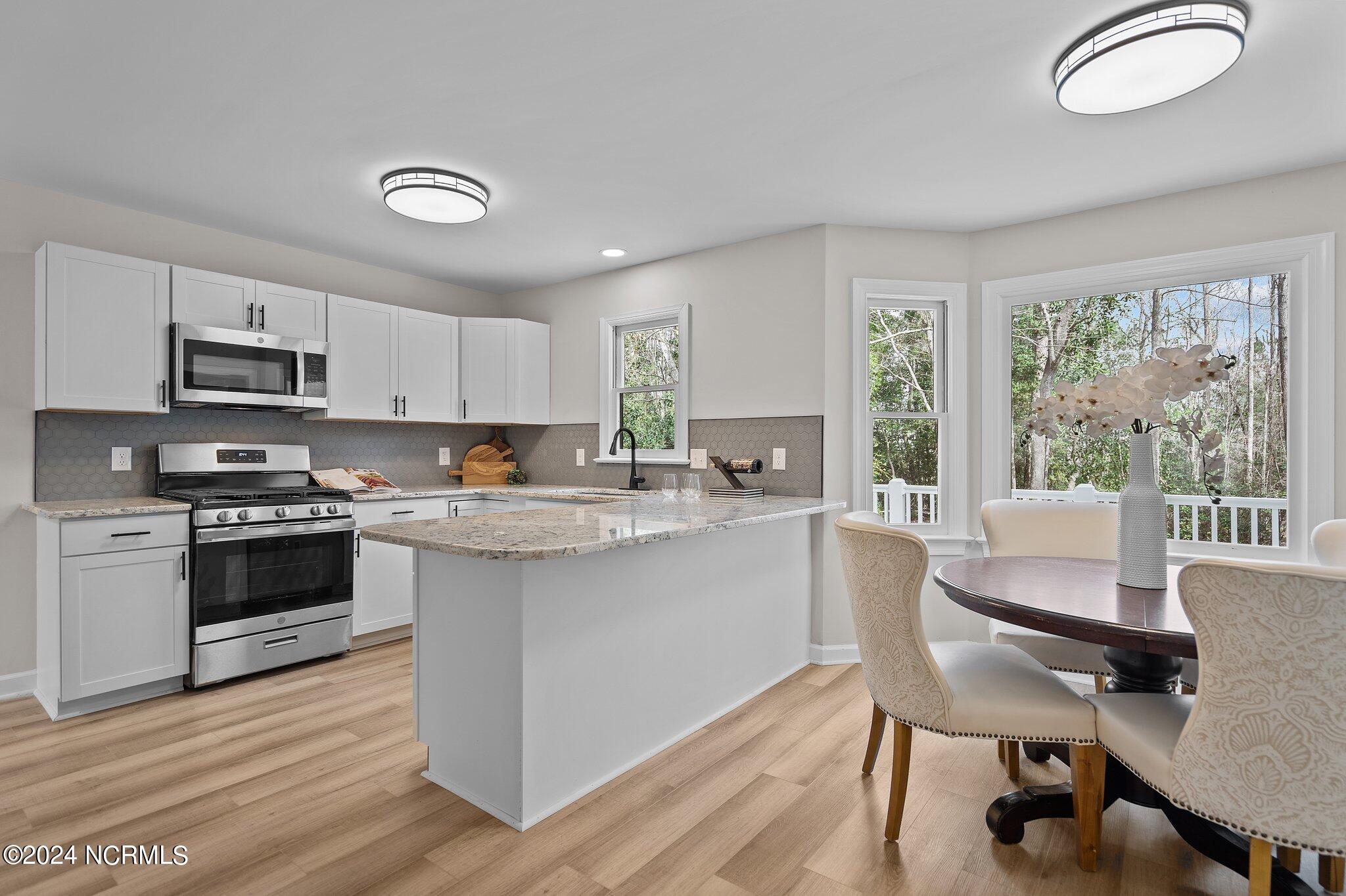 Bright kitchen with white cabinetry, stone island, stainless appliances, and an adjoining dining area.